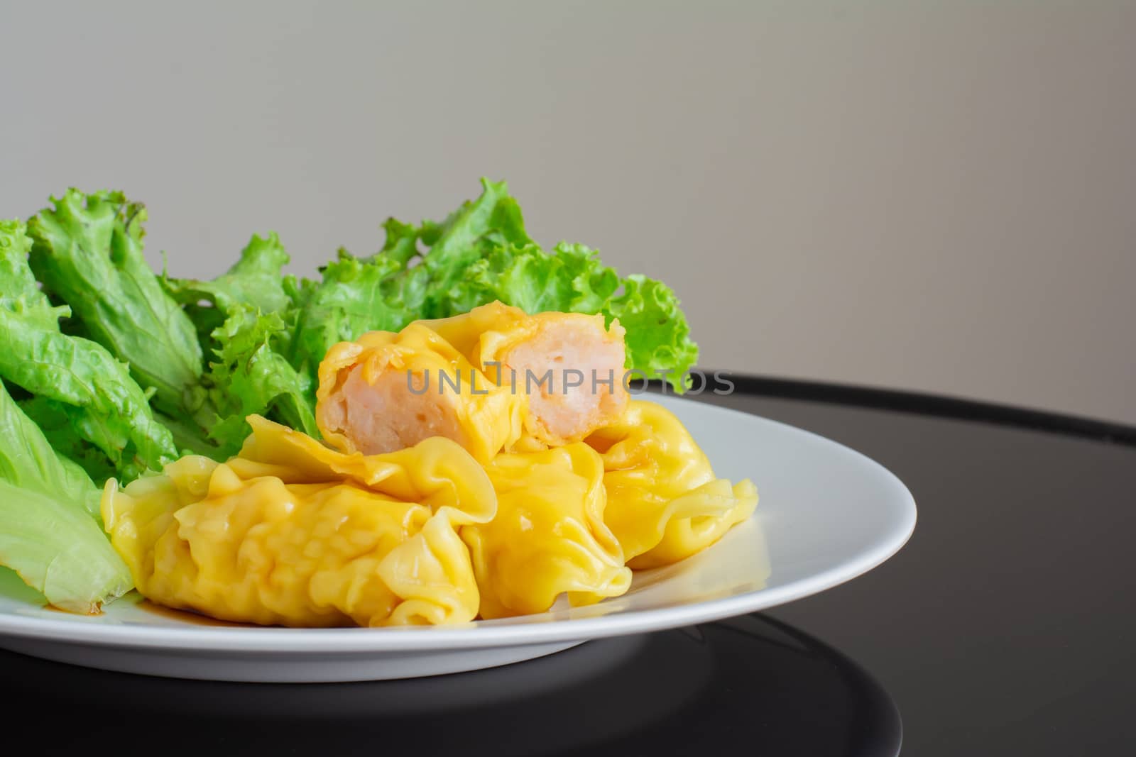 Steamed pork and shrimp on white plate with green lettuce on dark table. Delicious Chinese food. Dumpling in restaurant.