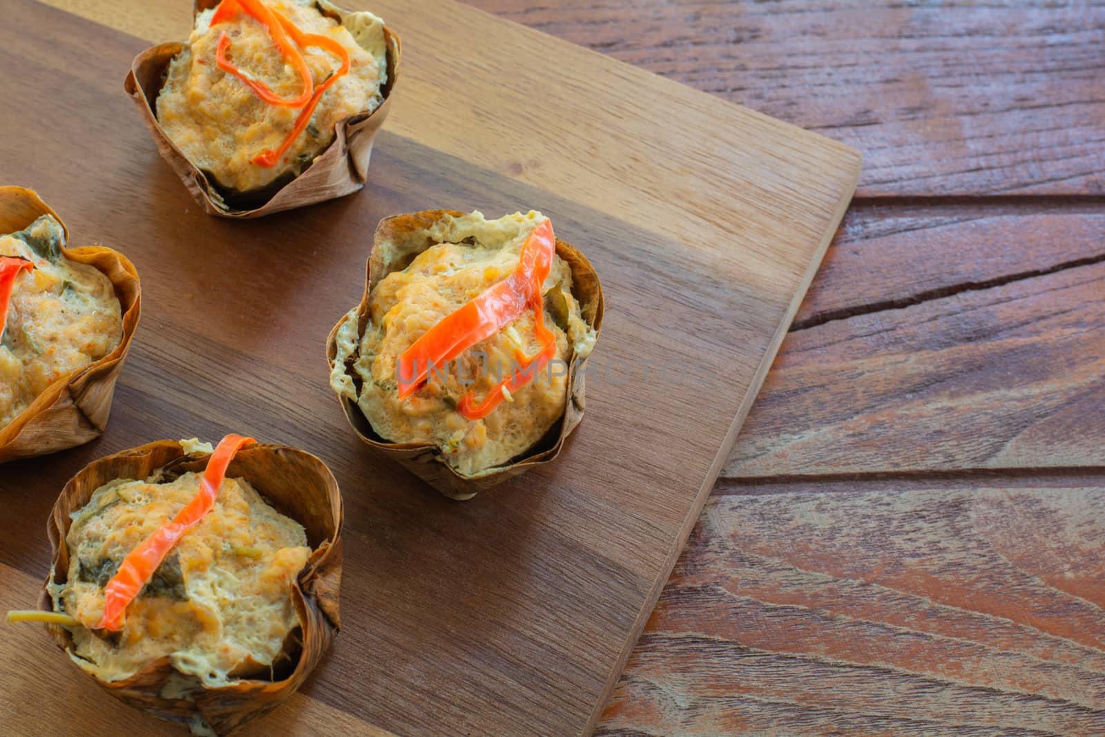 Thai steamed seafood curry in cup made from dry banana leave on wooden table and red chilli topping. Delicious Thai food.