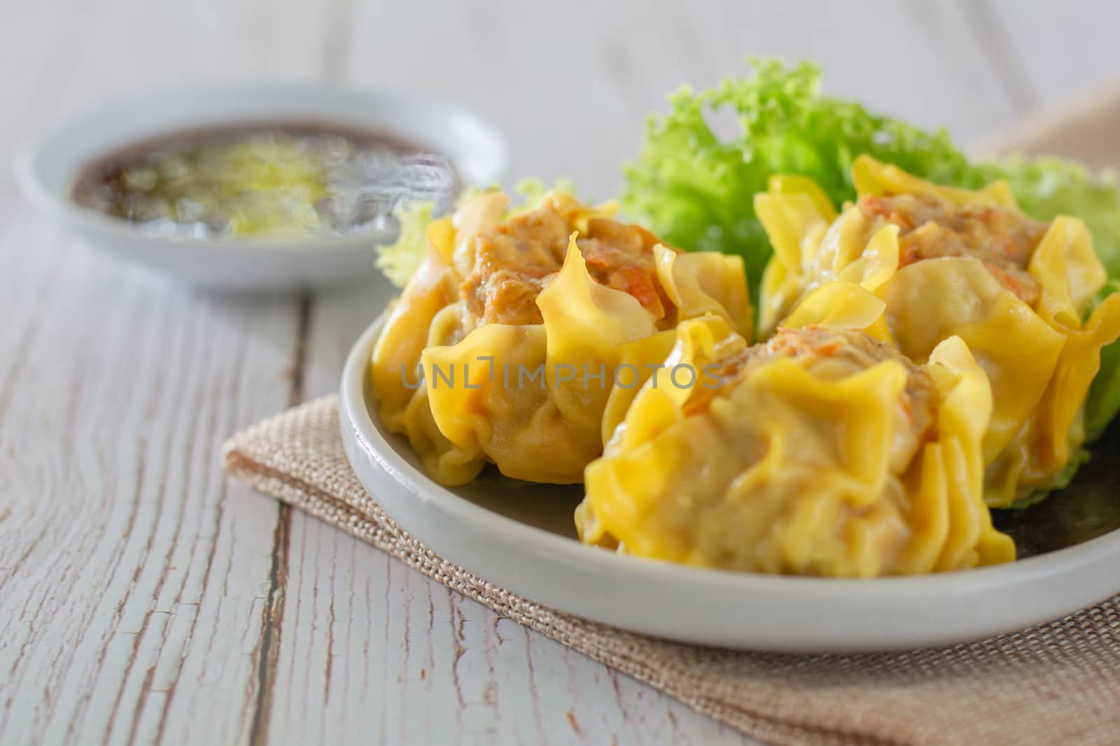 Chinese Steamed Dumpling, Shumai on white dish served with soy sauce and 
lettuce leaves on brown cloth and wooden table. Delicious Dimsum pork.