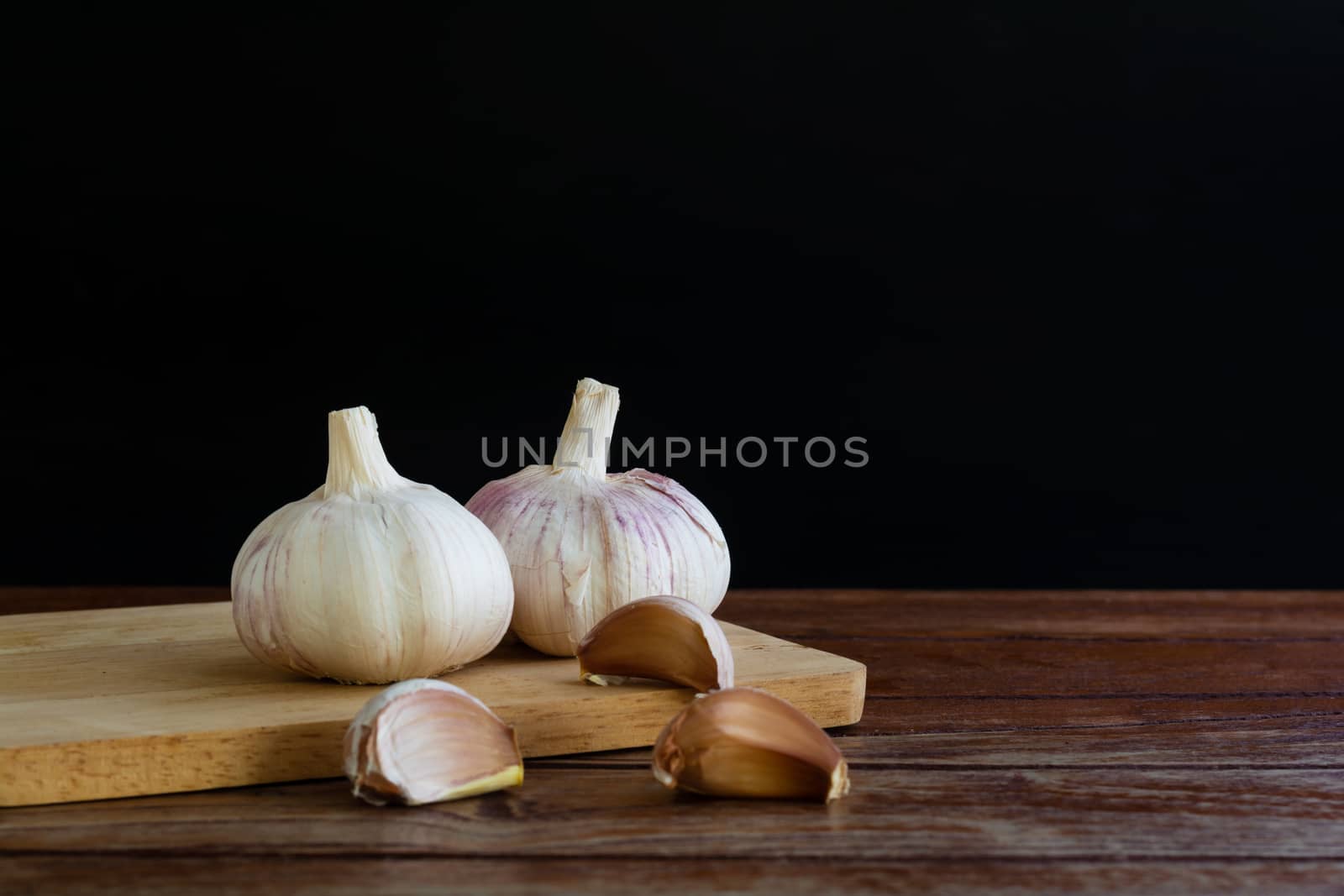 Group of garlic on chopping board and wooden table with black background. Copy space for your text.