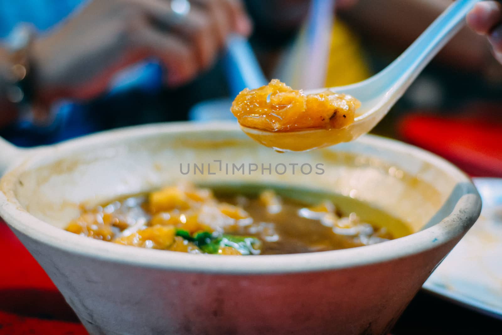 Eatting braised fish maw in red gravy in white ceramic bowl with white spoon served in restaurant at China town in Thailand. Selective Focusing.