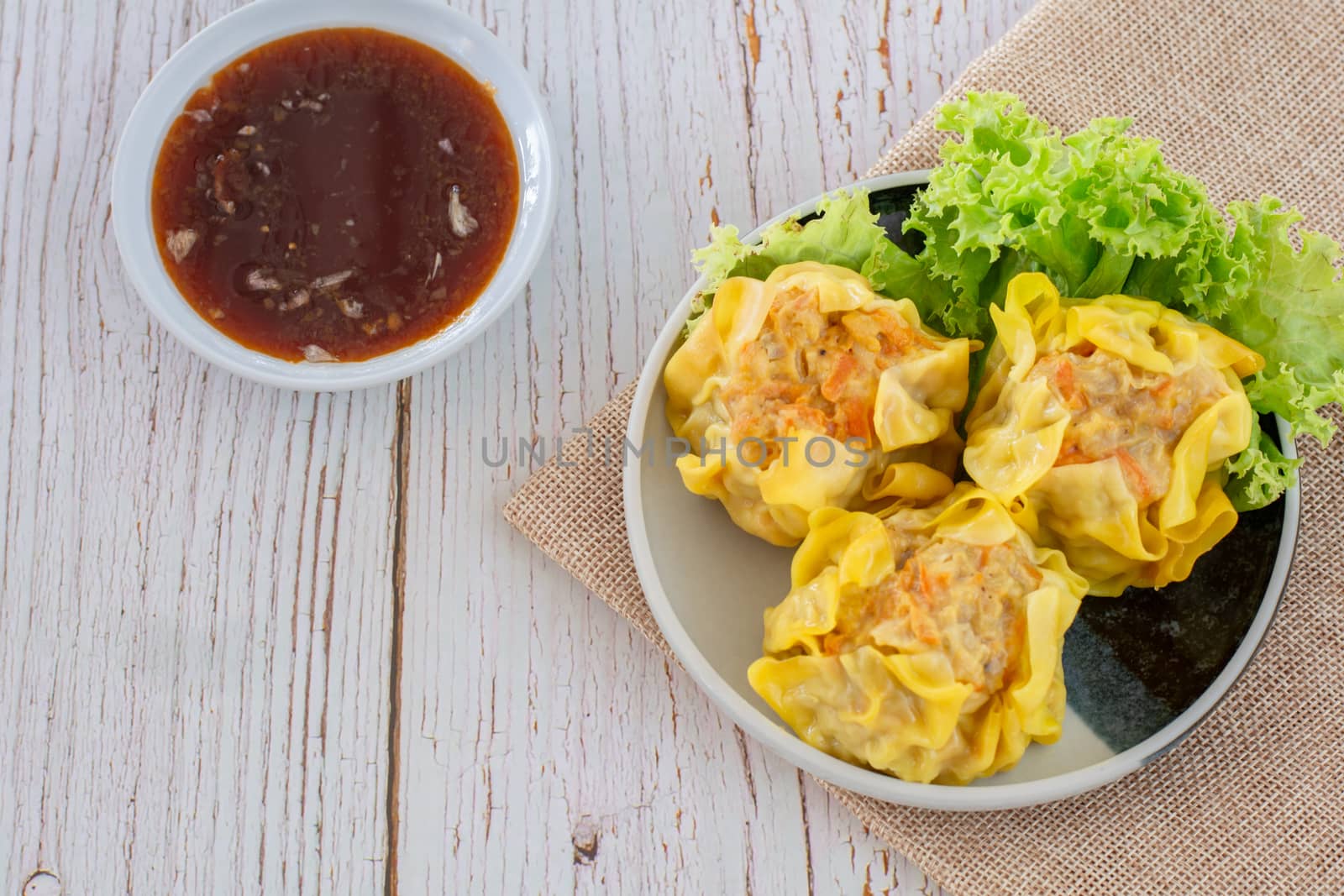 Chinese Steamed Dumpling, Shumai on white dish served with soy sauce and 
lettuce leaves on brown cloth and wooden table. Delicious Dimsum pork.