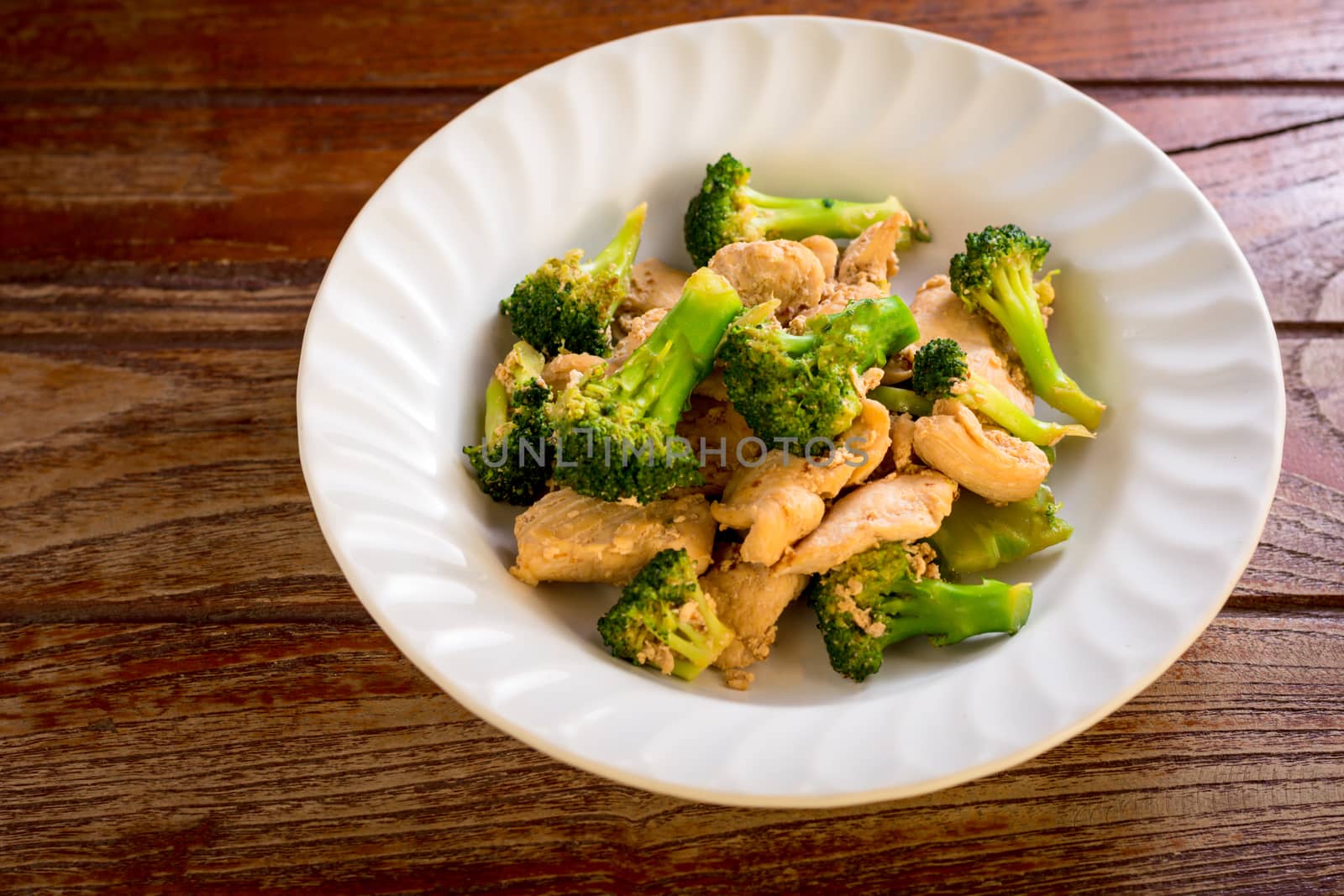 Stir fried broccoli and chicken in white plate on wooden table.