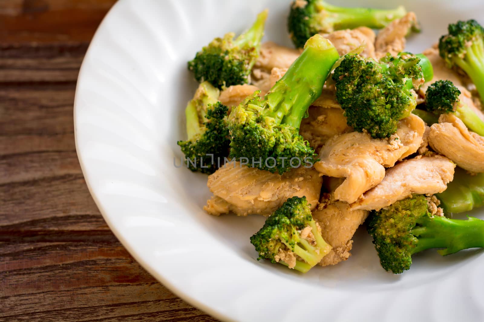 Top view stir fried broccoli and chicken in white plate on wooden table.