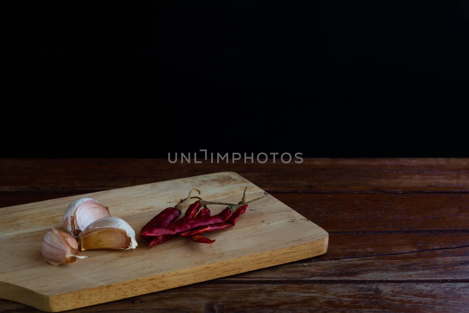 Group of garlic on chopping board and red dried chilli on wooden table with black background. Copy space for your text.