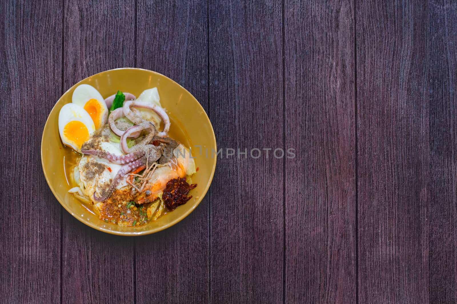 Delicious Thai food. Noodle with hot and sour seafood (prawn and squid) soup with slice boiled egg and vegetable in brown bowl at cafe and restaurant on wooden table.