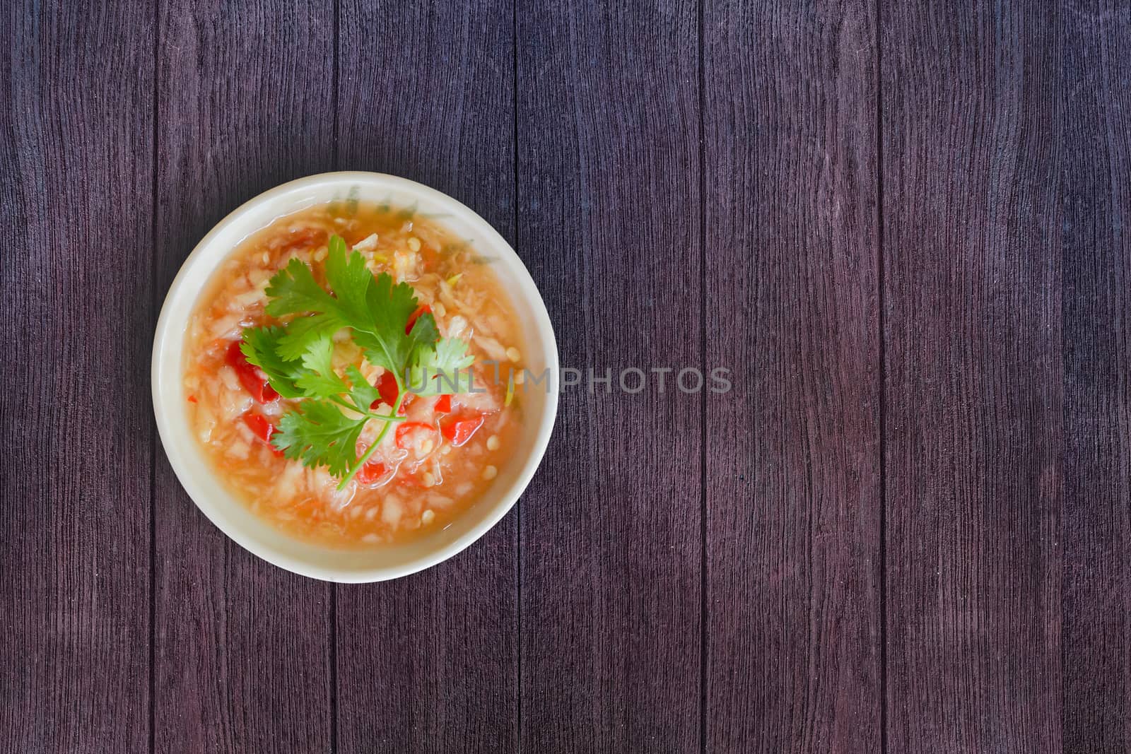 Top view Thai seafood dipping sauce in white bowl. Make from garlic, red chilli, fish sauce, salt, sugar, lime juice and coriander topping on dark wooden texture for background. Copy space for your text.