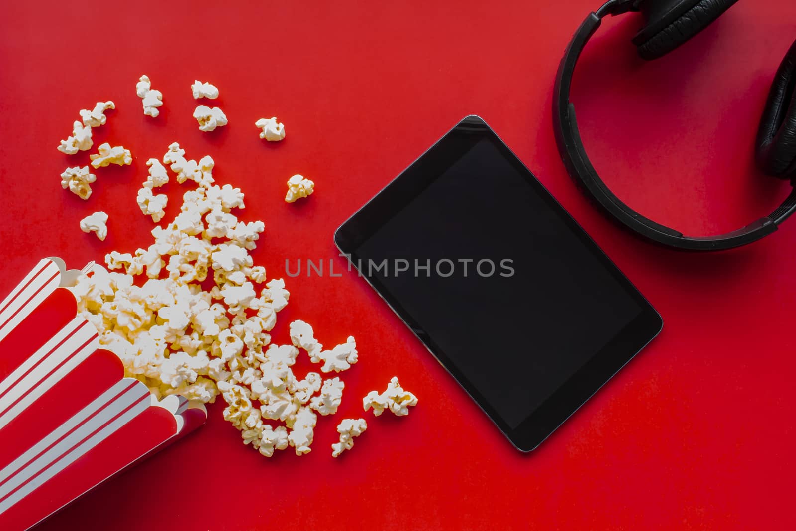 A tablet on a red background with popcorn and headphones by oasisamuel