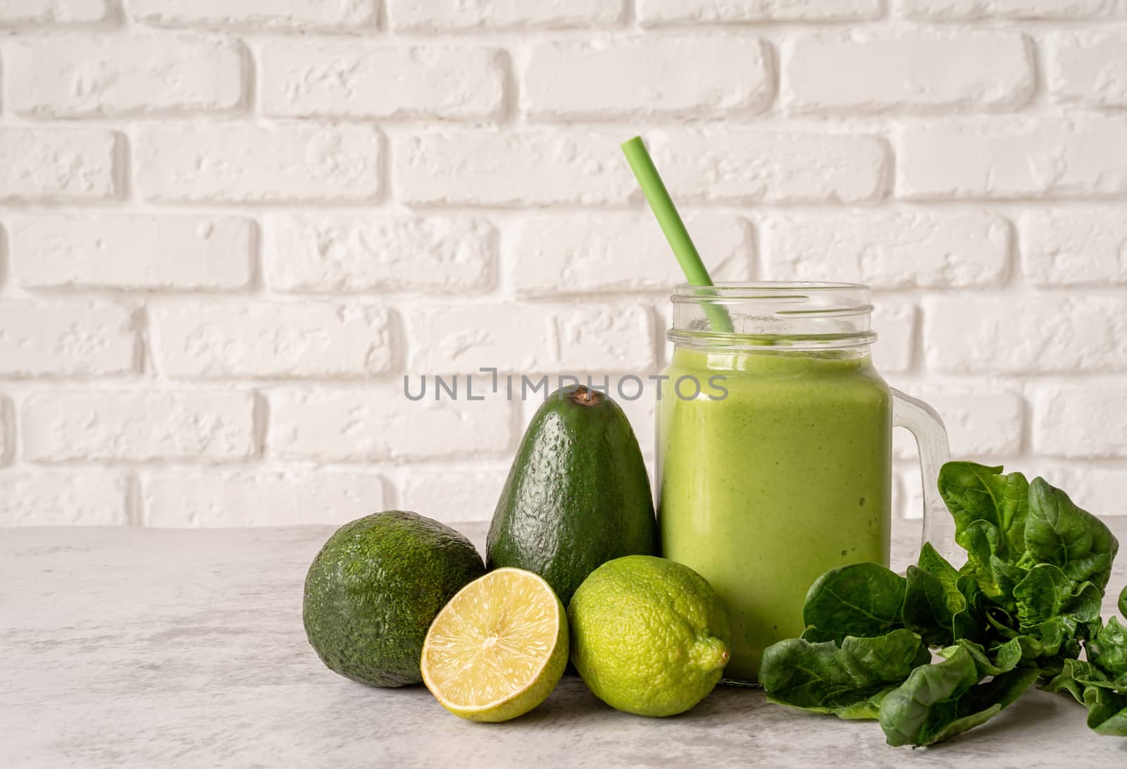 Avocado, lime and spinach smoothie in mason jar decorated with ingredients front view on white brick wall background