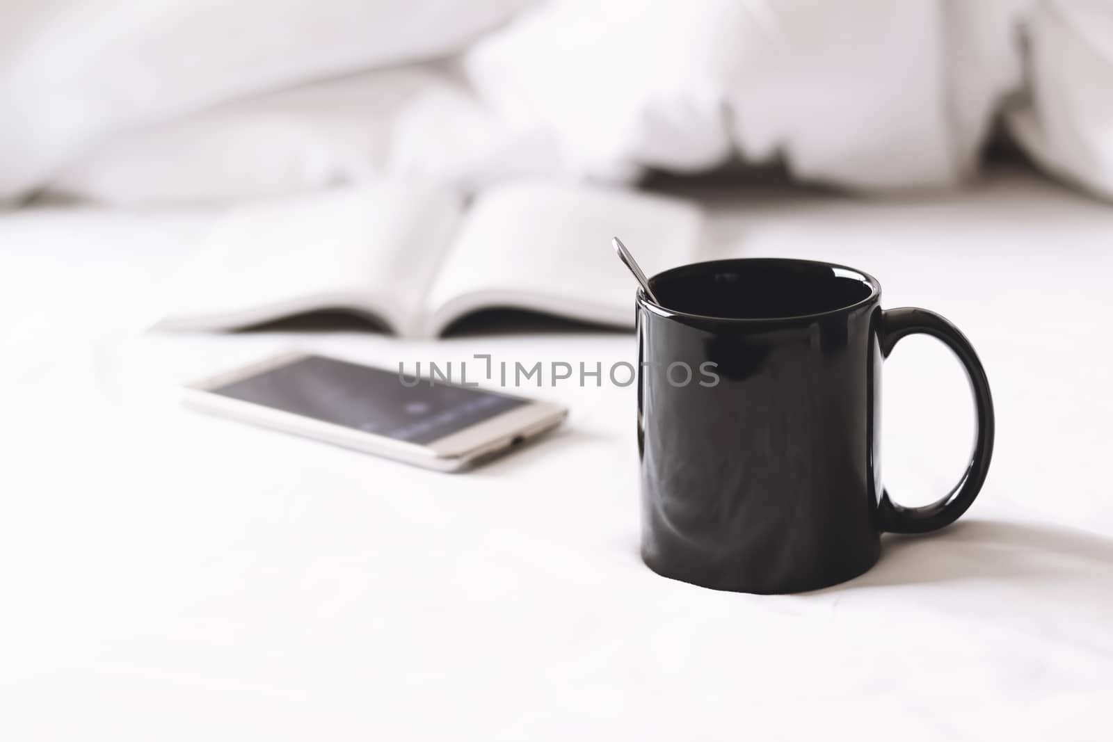 a coffee cup with smartphone and a book on bed by winnond