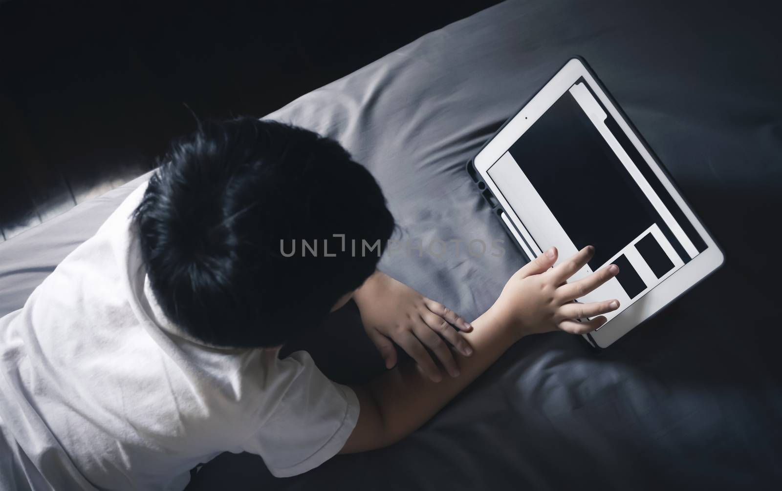 create a schedule routine for children to use their screen. tablet could have a lot of games and educational apps to help kids learn. boy using a tablet and watching on the bed while staying at home.