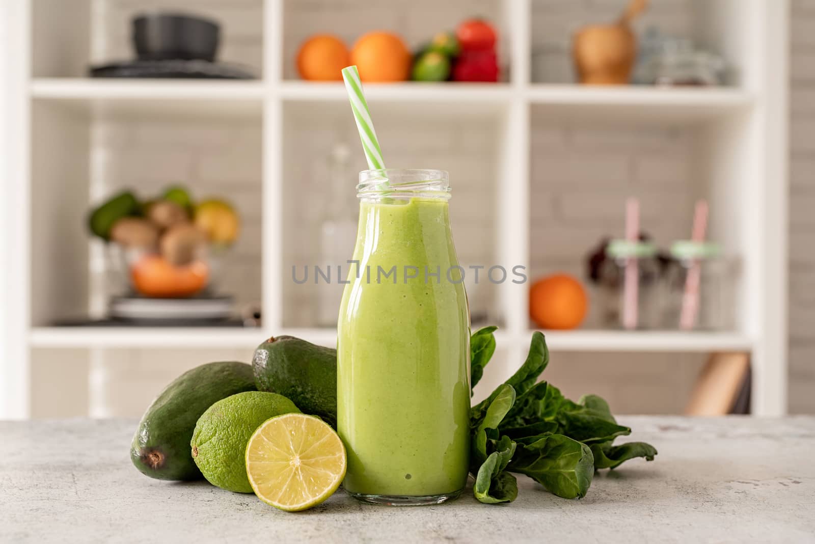 Avocado, lime and spinach smoothie in glass bottle front view on home kitchen background