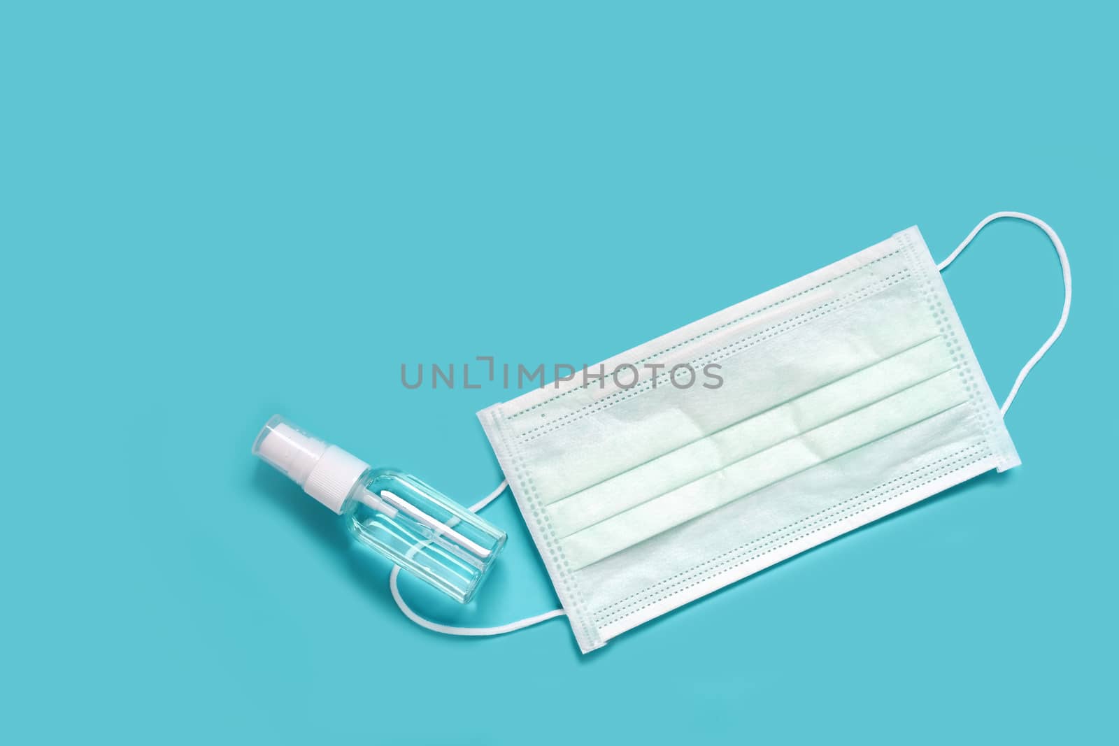 medical face mask and disinfectant alcohol sanitizer spray to prevent coronavirus disease. products to protect from germs when on the go. blue background for text.