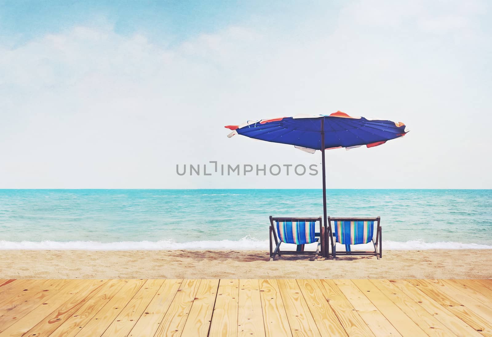 wooden floor in the foreground and beach chairs with parasol on sand (retro filter)