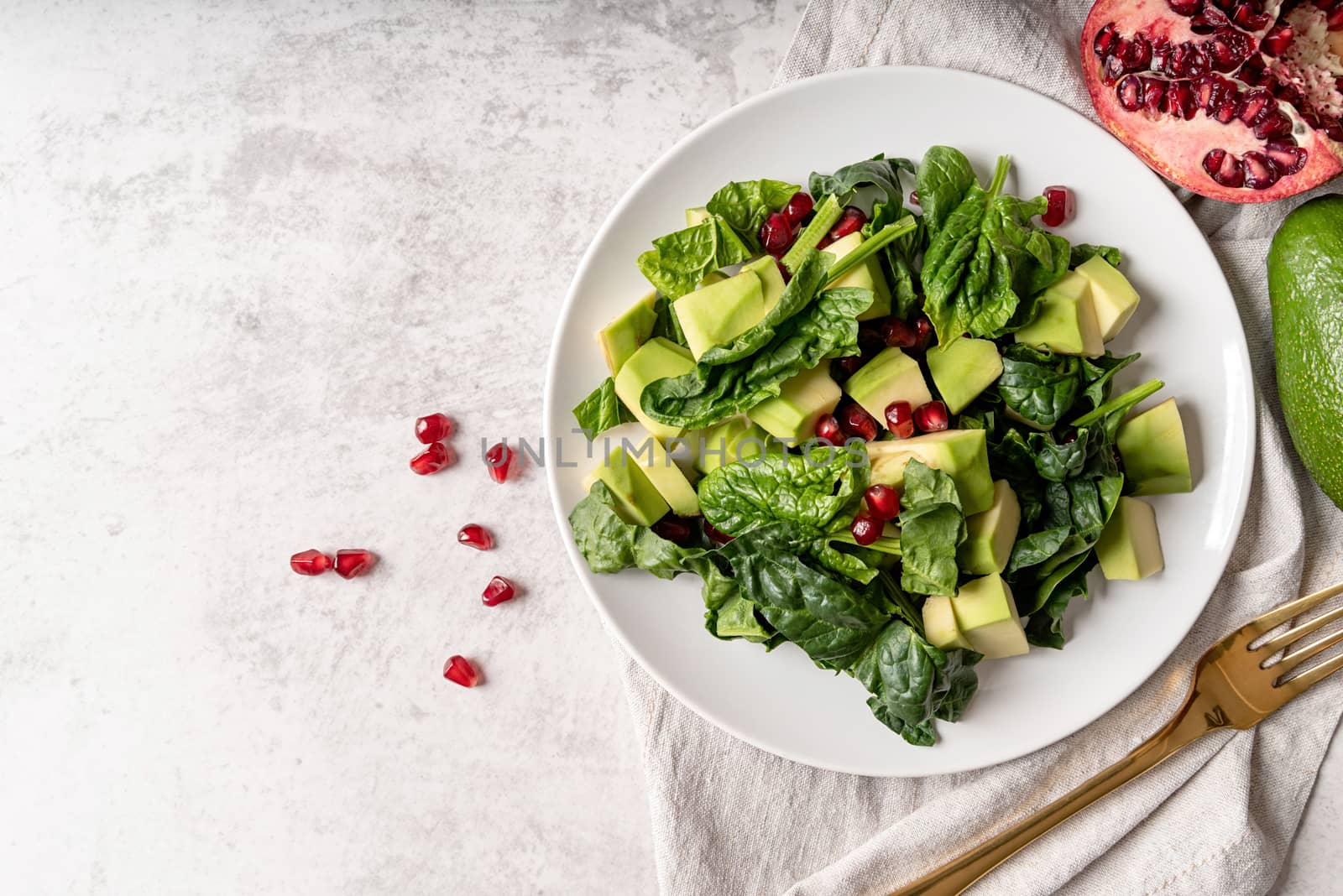Healthy food concept. Fresh salad with avocado, spinach and pomegranate top view on white background with copy space