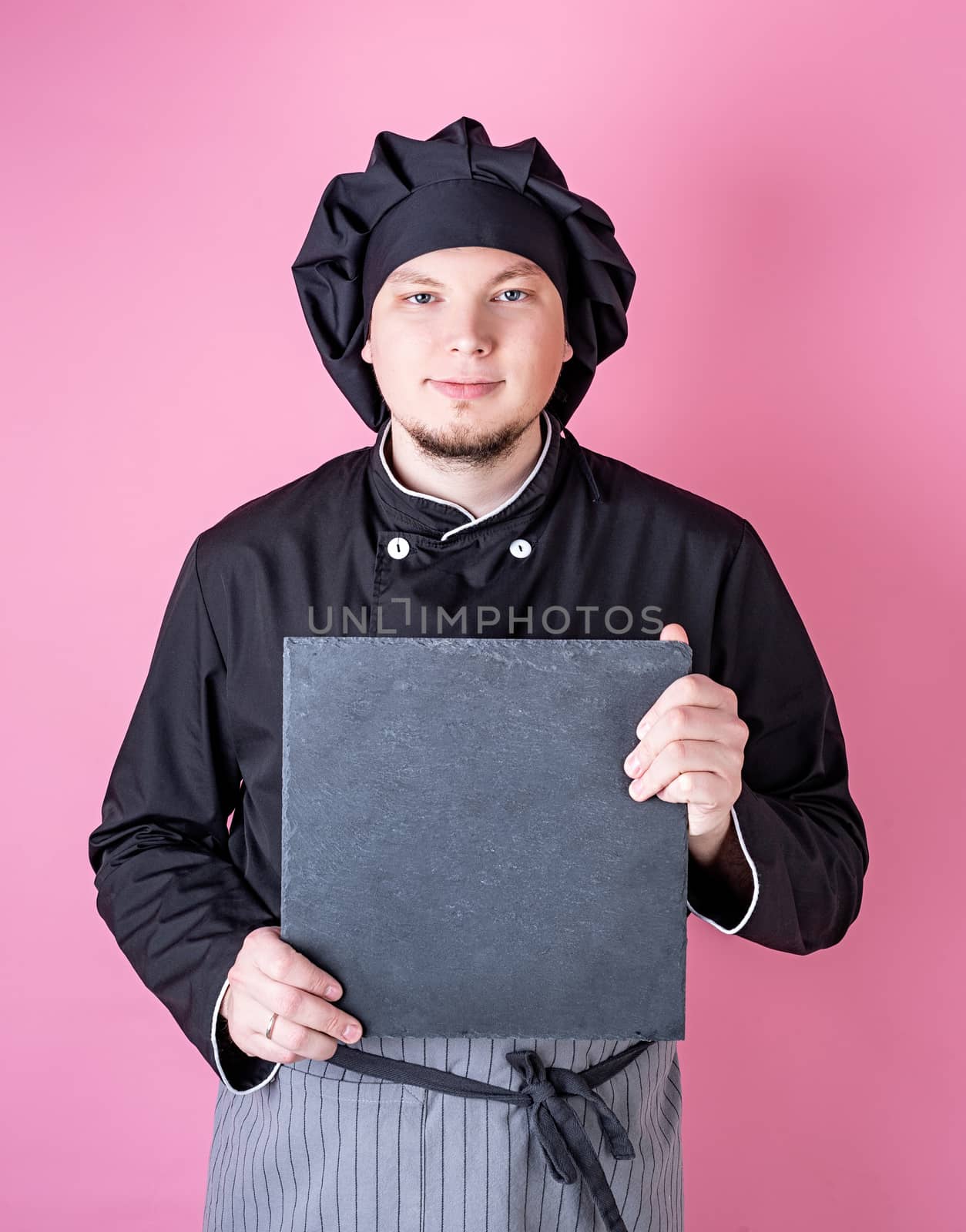 Male chef holding a square board isolated on pink with copy space by Desperada