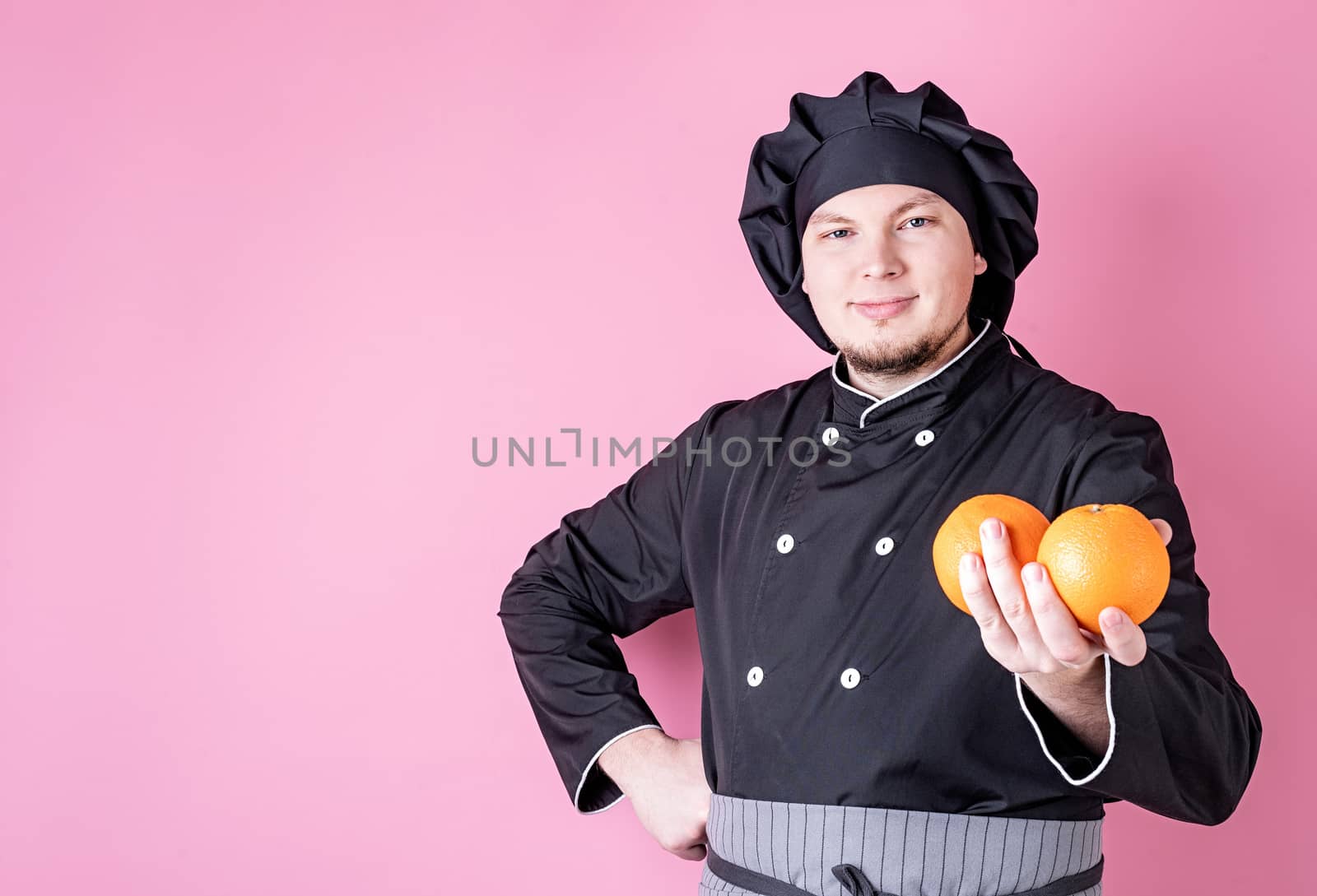 Young smiling male chef holding oranges isolated on pink background with copy space
