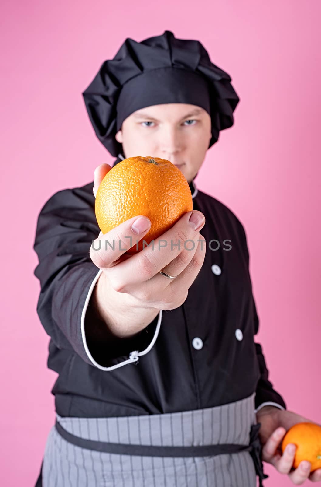Young smiling male chef holding oranges isolated on pink background with copy space. Selective focus