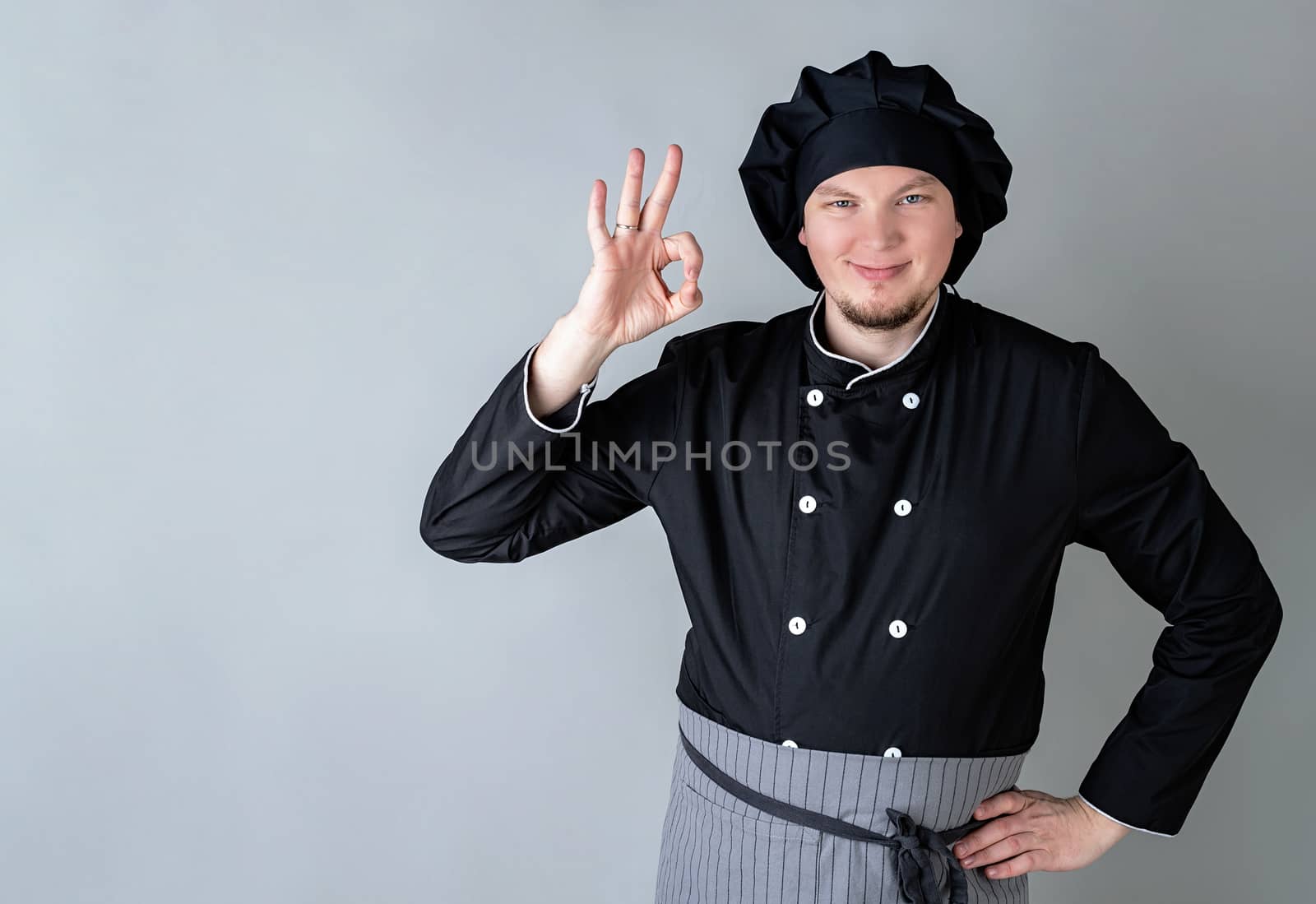 Young smiling male chef showing ok sign isolated on gray background with copy space
