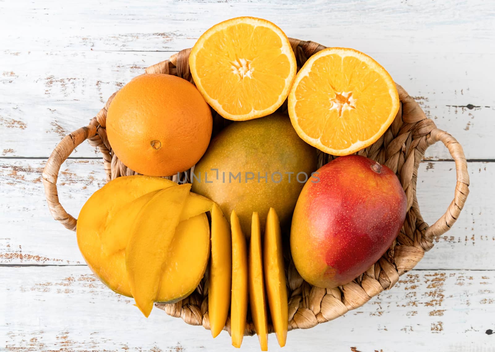 Still life of tropical fruit in basket top view on white wooden background