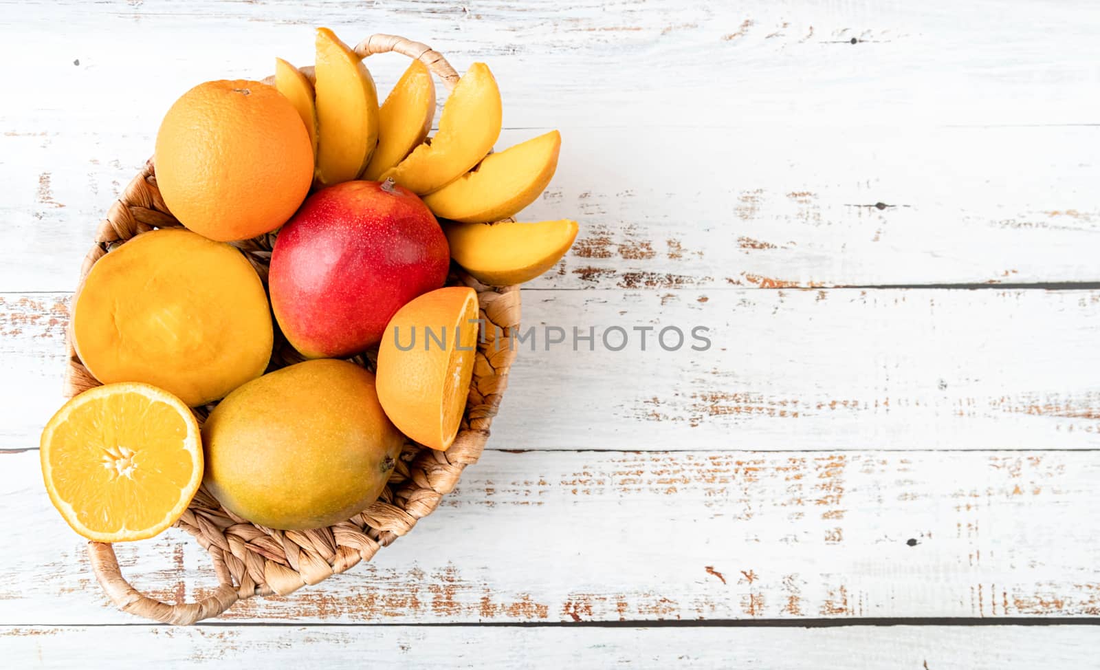 Still life of tropical fruit in basket top view on white wooden background with copy space