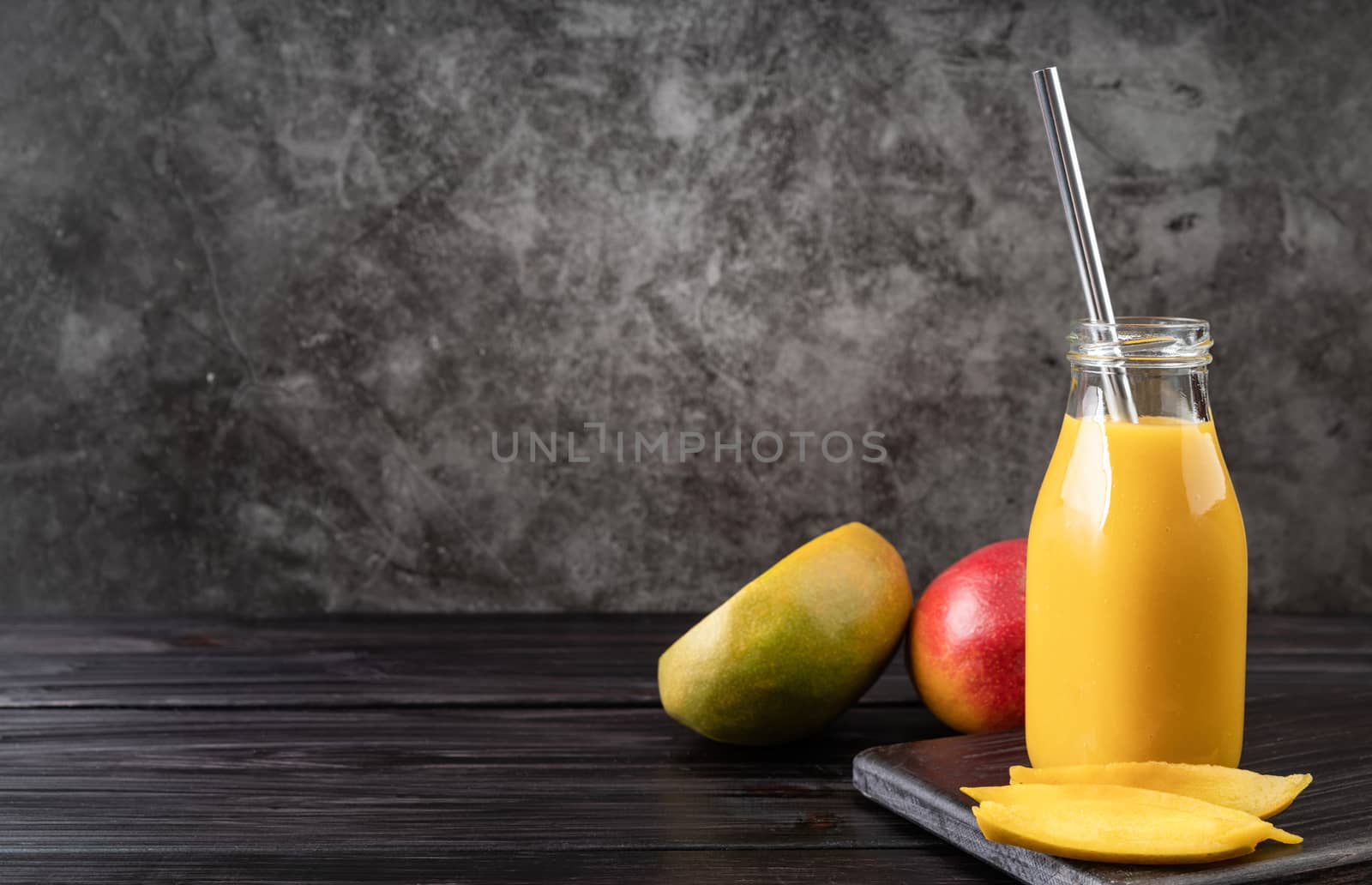 fresh mango shake in a glass with a metal drinking straw decorated with slices of mango front view on dark wooden background by Desperada