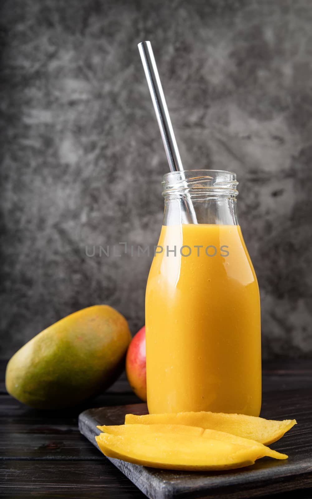fresh mango shake in a glass with a metal drinking straw decorated with slices of mango front view on dark wooden background
