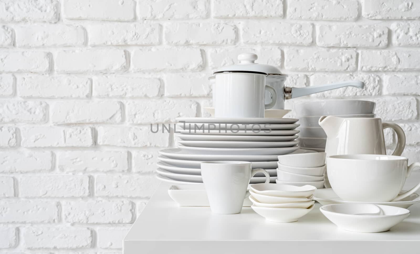 stack of white ceramic dishes and tableware on the table on white brick wall background by Desperada