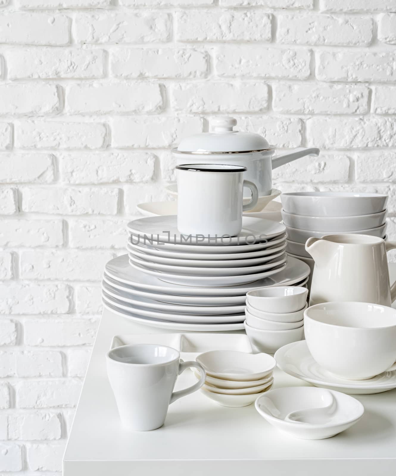 piles of white ceramic dishes and tableware on the table on white brick wall background by Desperada
