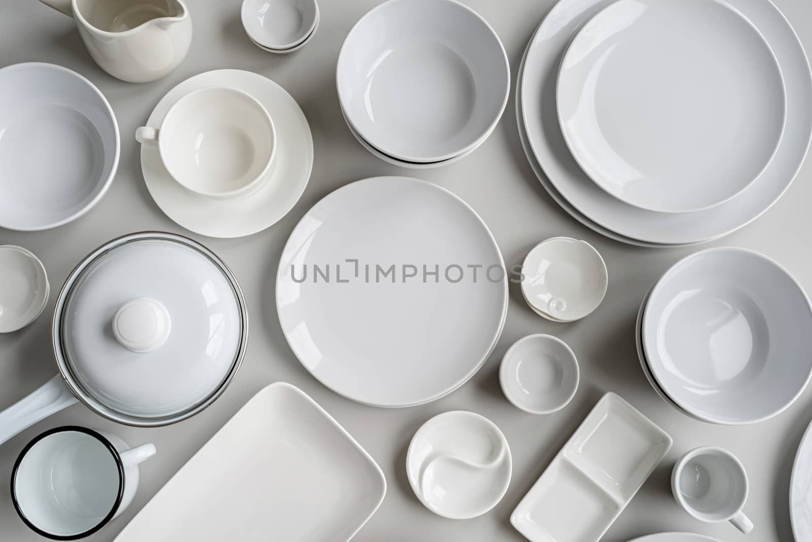 piles of white ceramic dishes and tableware top view on gray background by Desperada