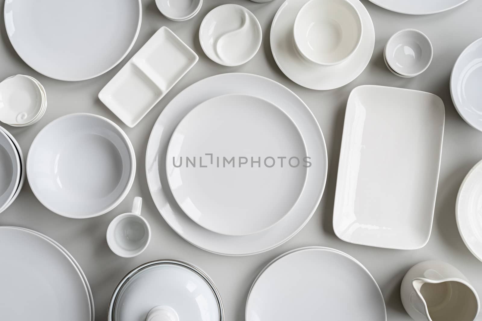 piles of white ceramic dishes and tableware top view on gray background by Desperada
