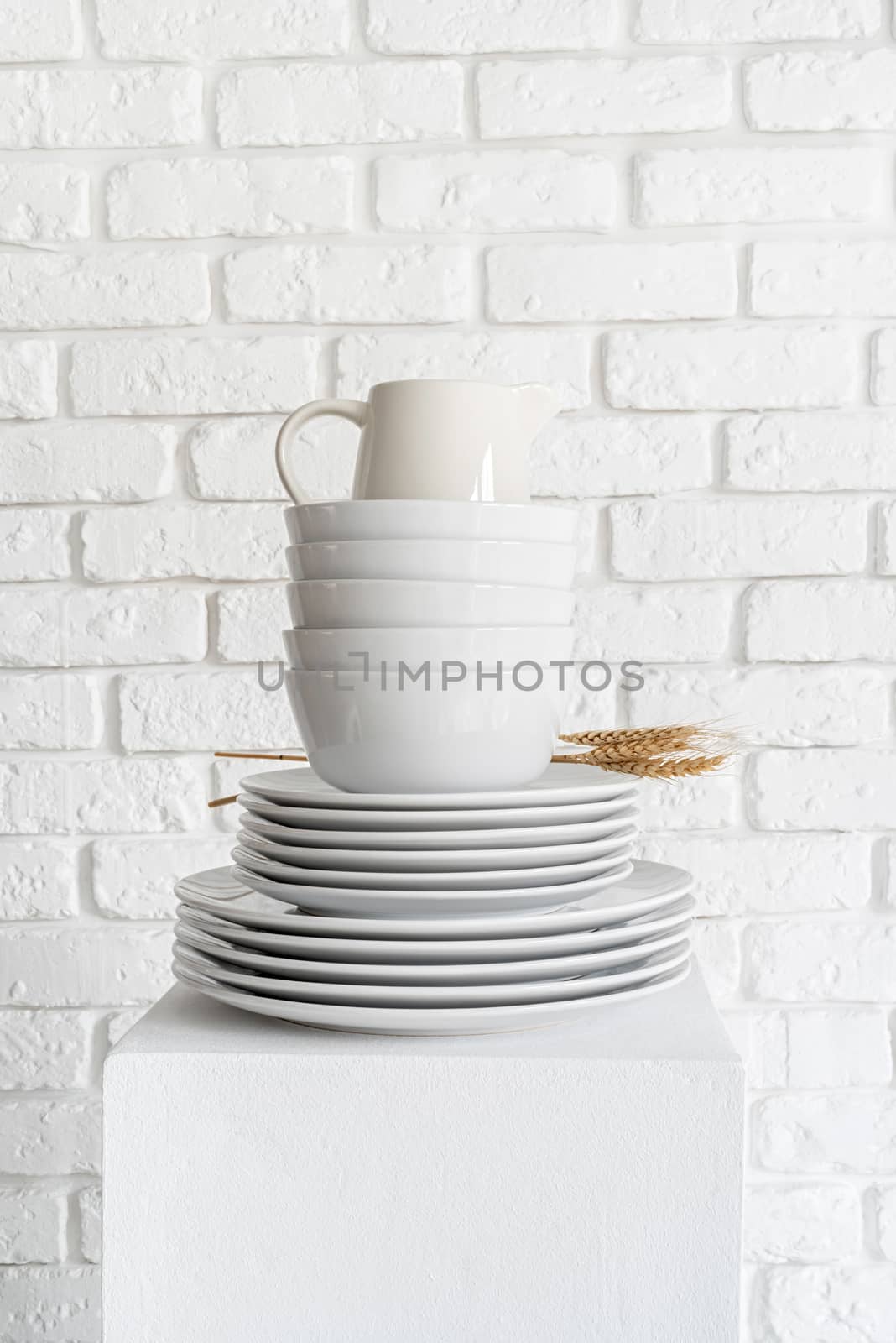 stack of white ceramic dishes and tableware on white brick wall background by Desperada