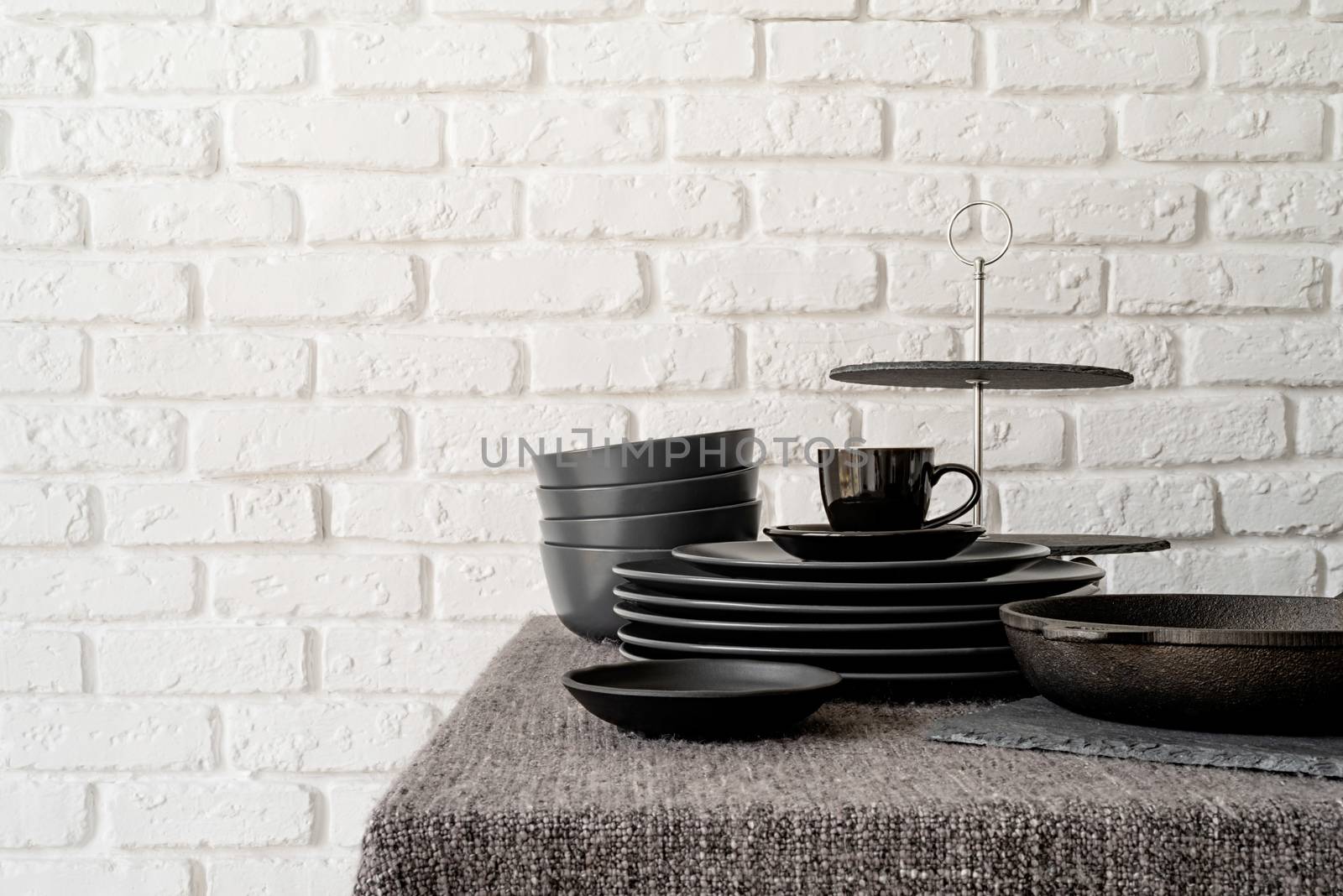 stack of black ceramic dishes and tableware on the table on white brick wall background with copy space