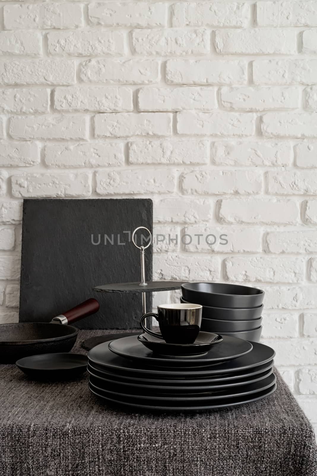 stack of black ceramic dishes and tableware on the table on white brick wall background with copy space