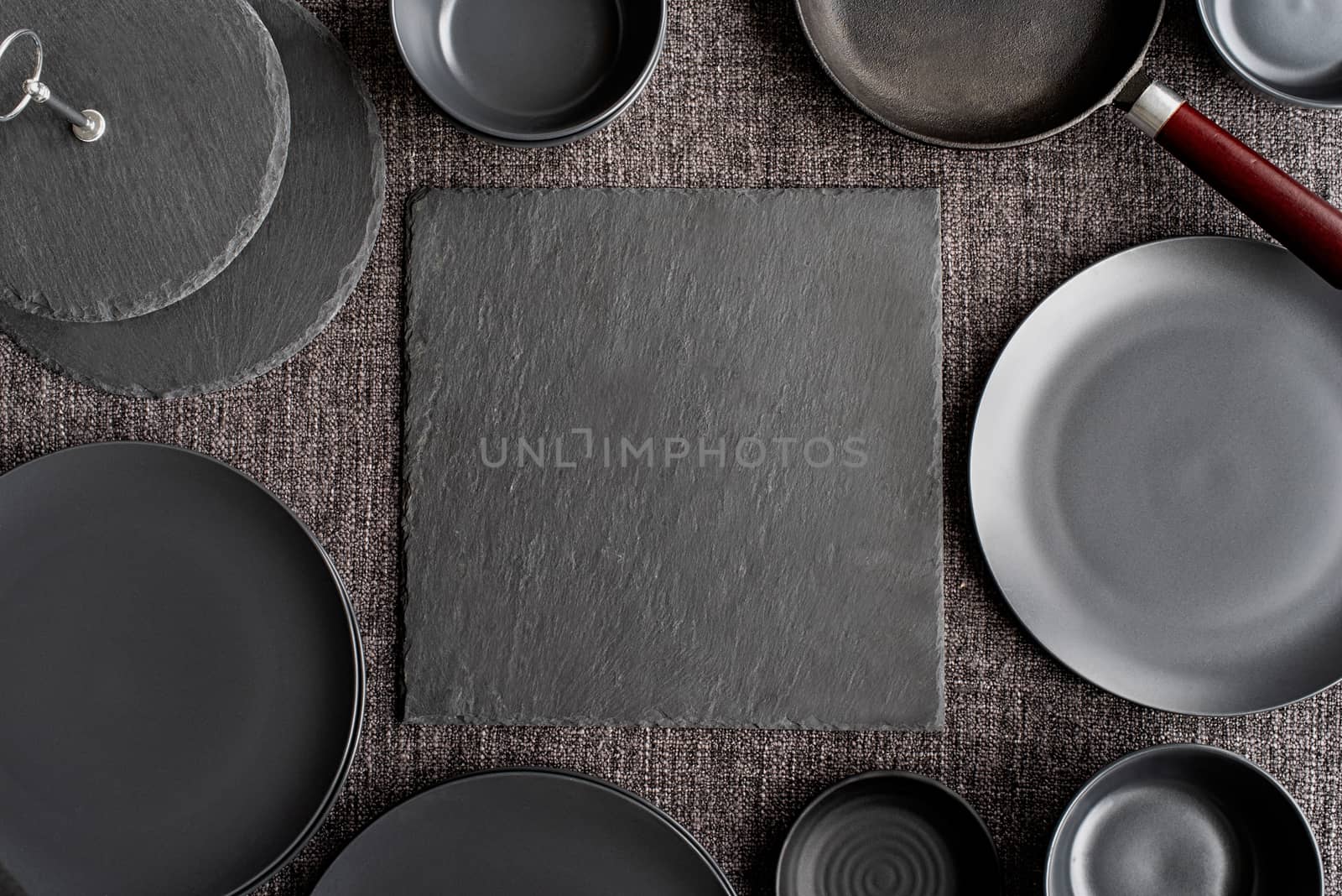 piles of black ceramic dishes and tableware top view on gray background by Desperada