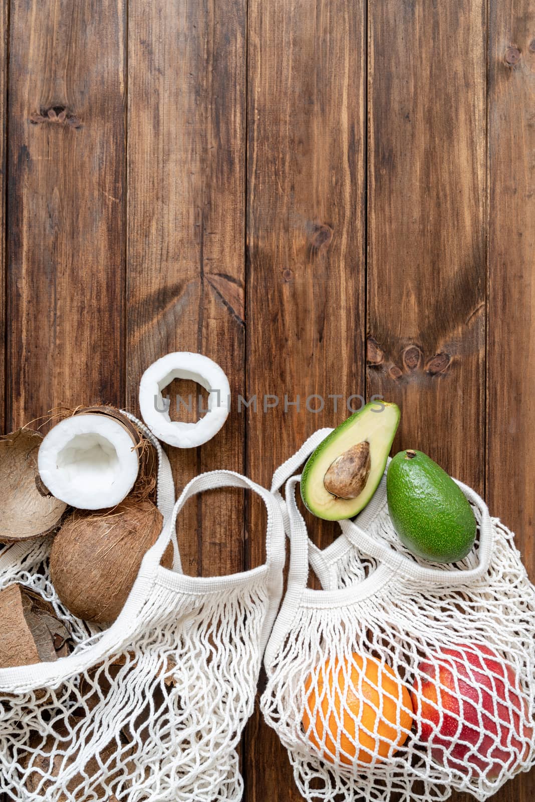 Summer fruit. Eco friendly shopping. Tropical fruit in white mesh bags top view flat lay on wooden background