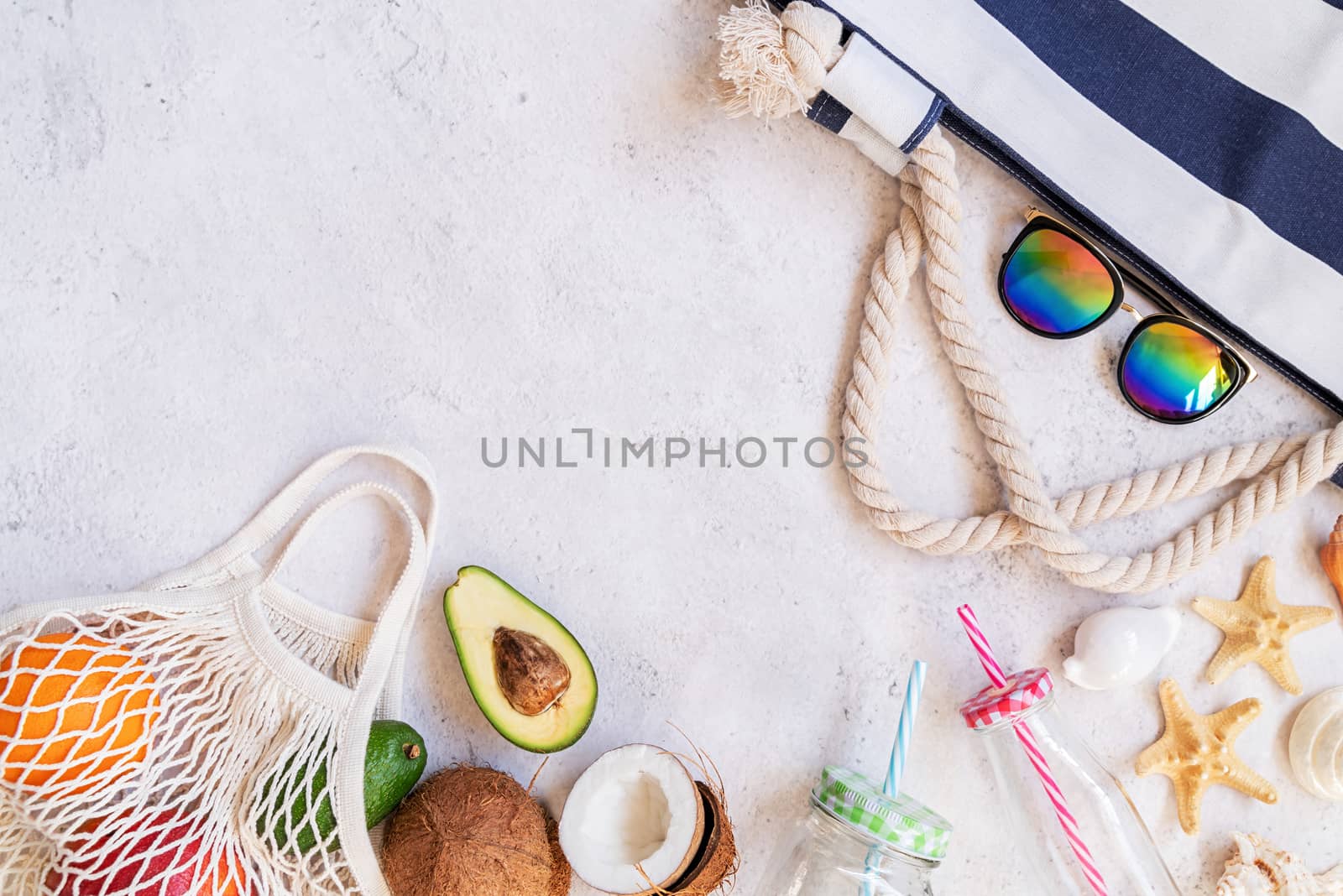 Summer vibes concept. Flat lay of mesh bags full of fruit, drinking glass, summer hat, sunglasses and starfish top view on white marble background with copy space