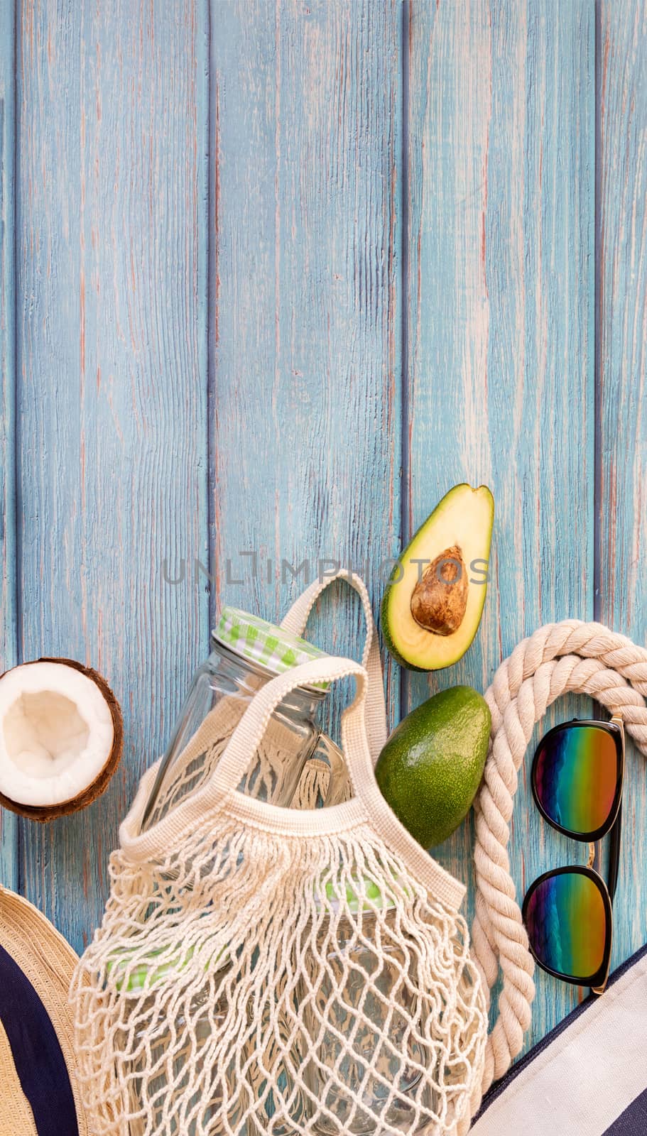 Summer vibes concept. Vacation concept. Mesh bag full of tropical fruit with sunglasses and beach hat top view flat lay on blue wooden background