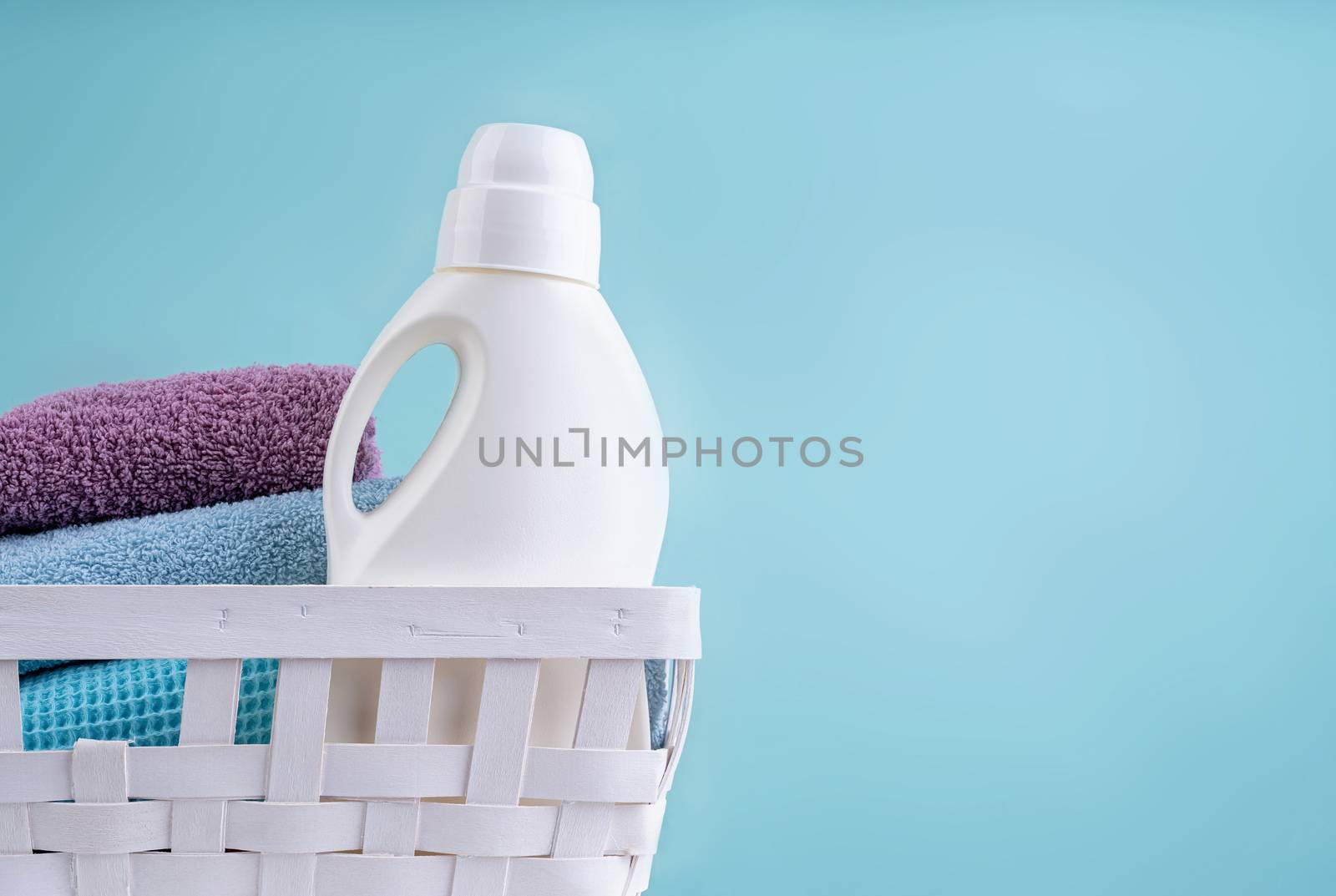 Laundry basket with a detergent bottle and a pile of clean towels on white table isolated on blue background by Desperada