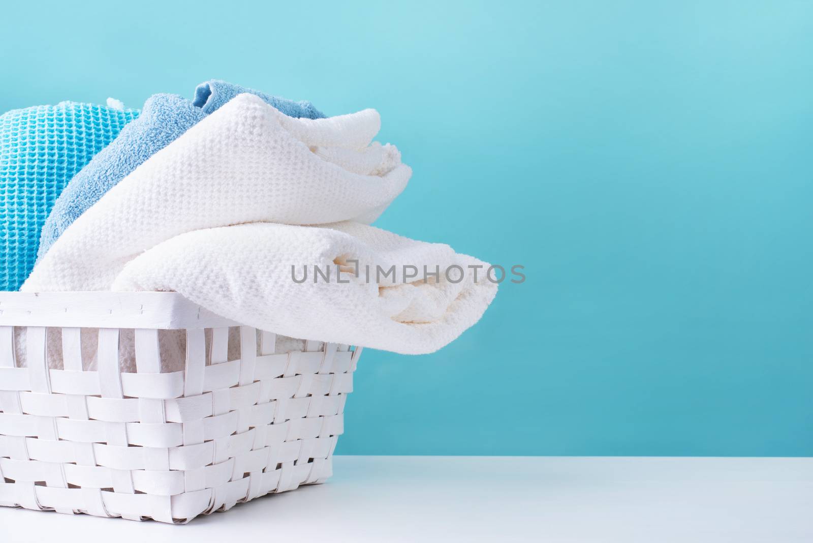 stack of clean towels in a white laundry basket on blue background by Desperada