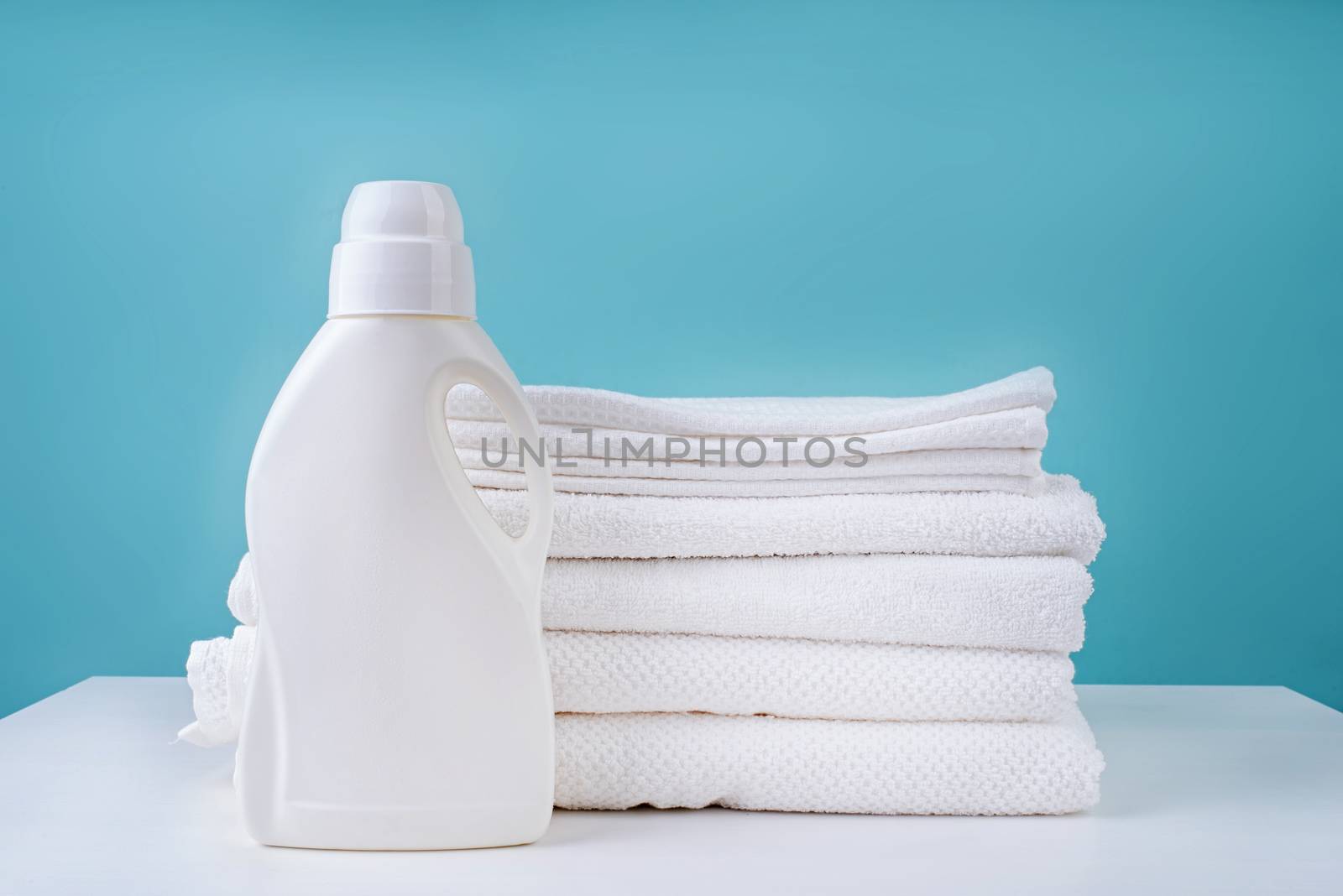 Laundry concept. Stack of clean white towels and a bottle of detergent on blue background with copy space