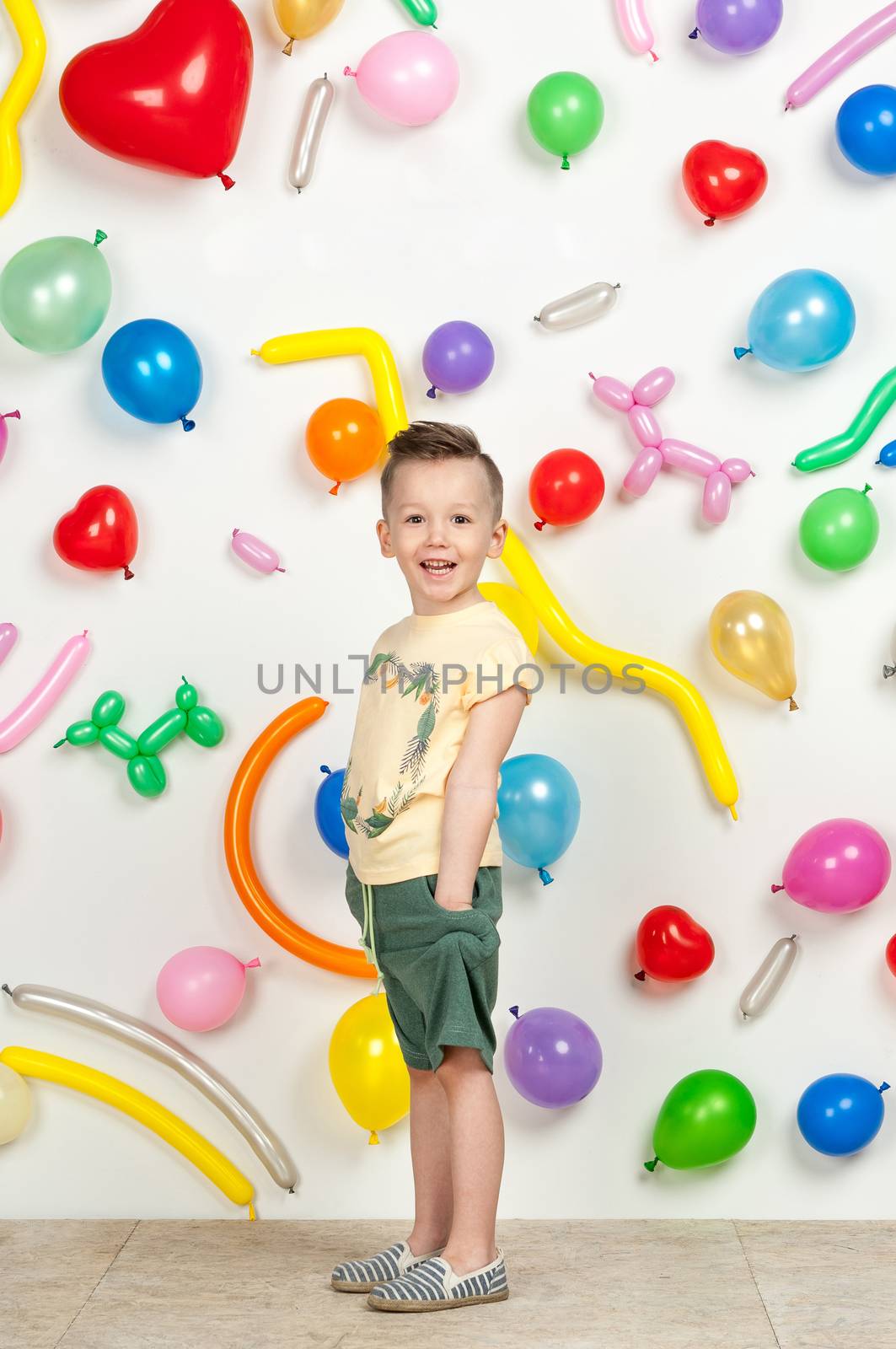 boy on a white background with colorful balloons. boy in a tank top and shorts on a white background with balloons in the shape of a heart