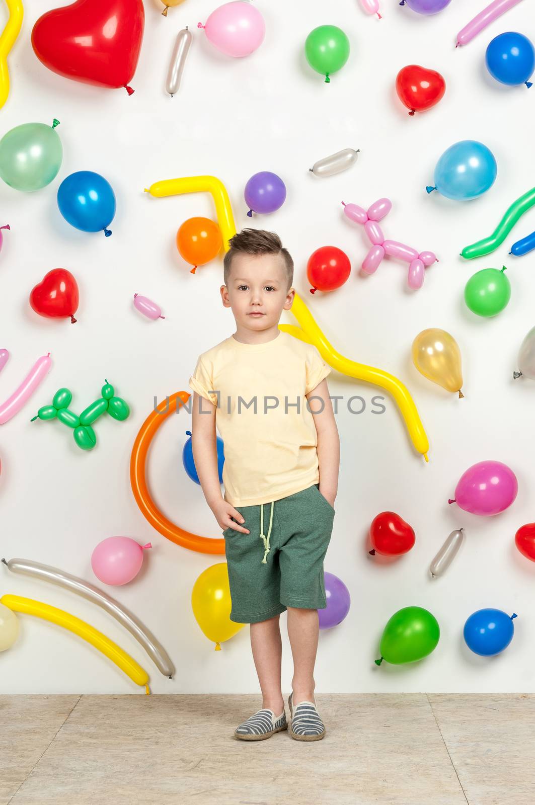 boy on a white background with colorful balloons. boy in a tank top and shorts on a white background with balloons in the shape of a heart