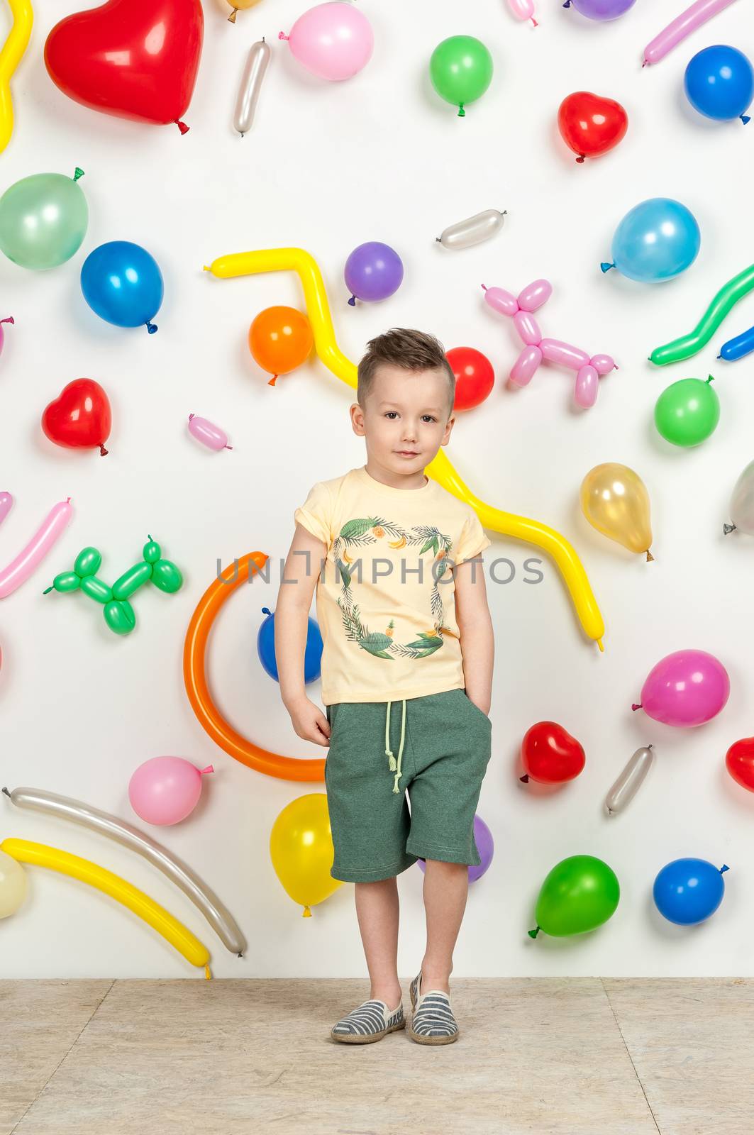 boy on a white background with colorful balloons. boy in a tank top and shorts on a white background with balloons in the shape of a heart