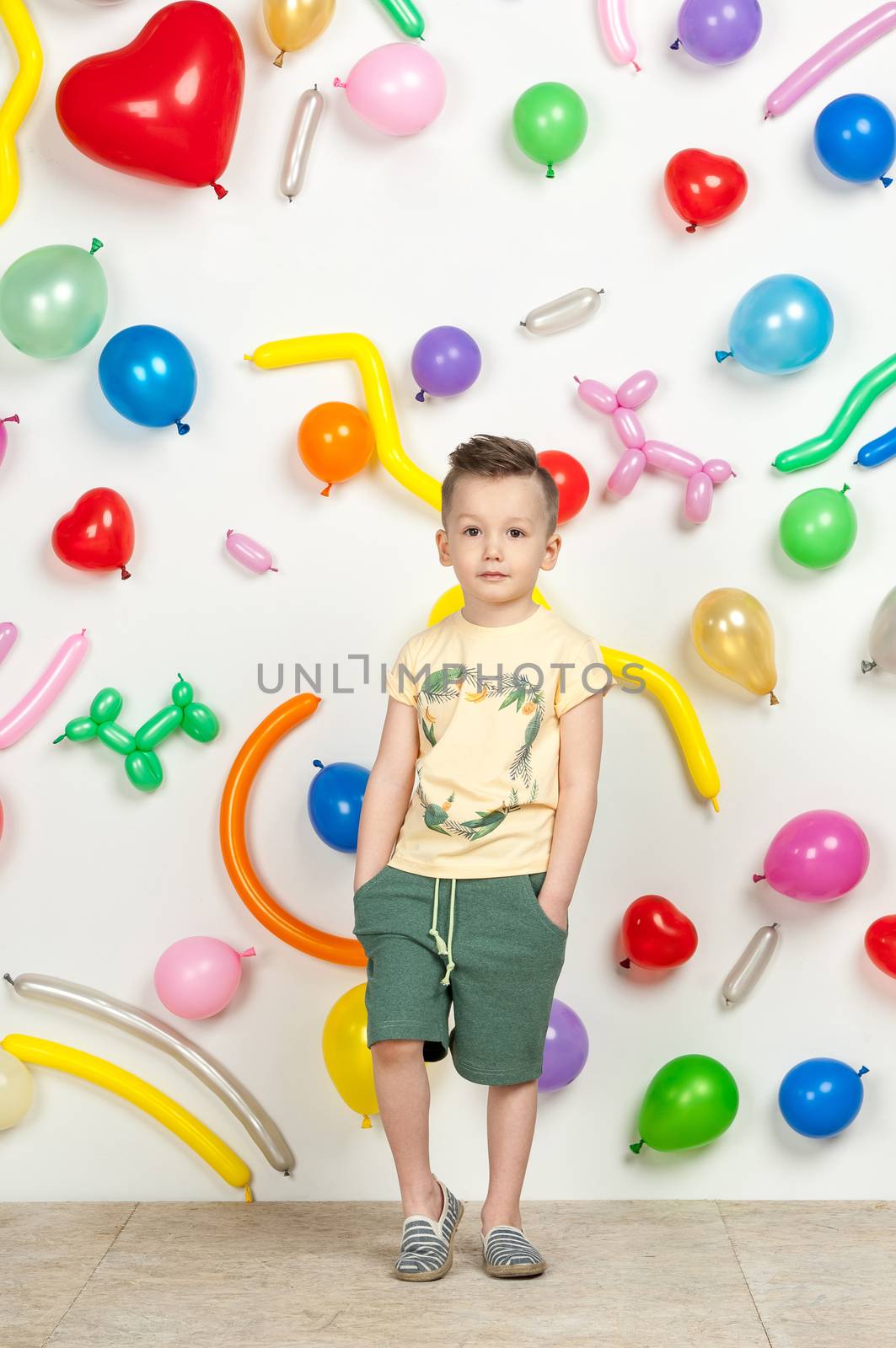 boy on a white background with colorful balloons. boy in a tank top and shorts on a white background with balloons in the shape of a heart