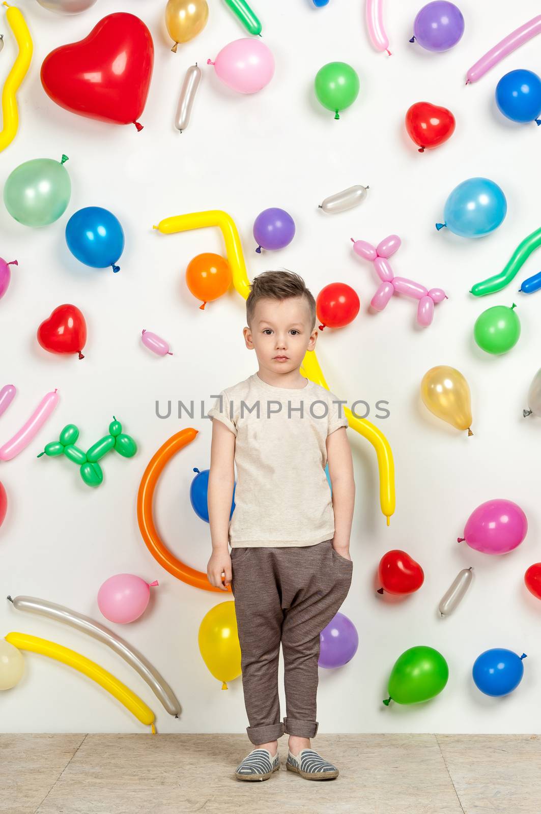 boy on a white background with colorful balloons. boy in a tank top and pants on a white background with balloons in the shape of a heart