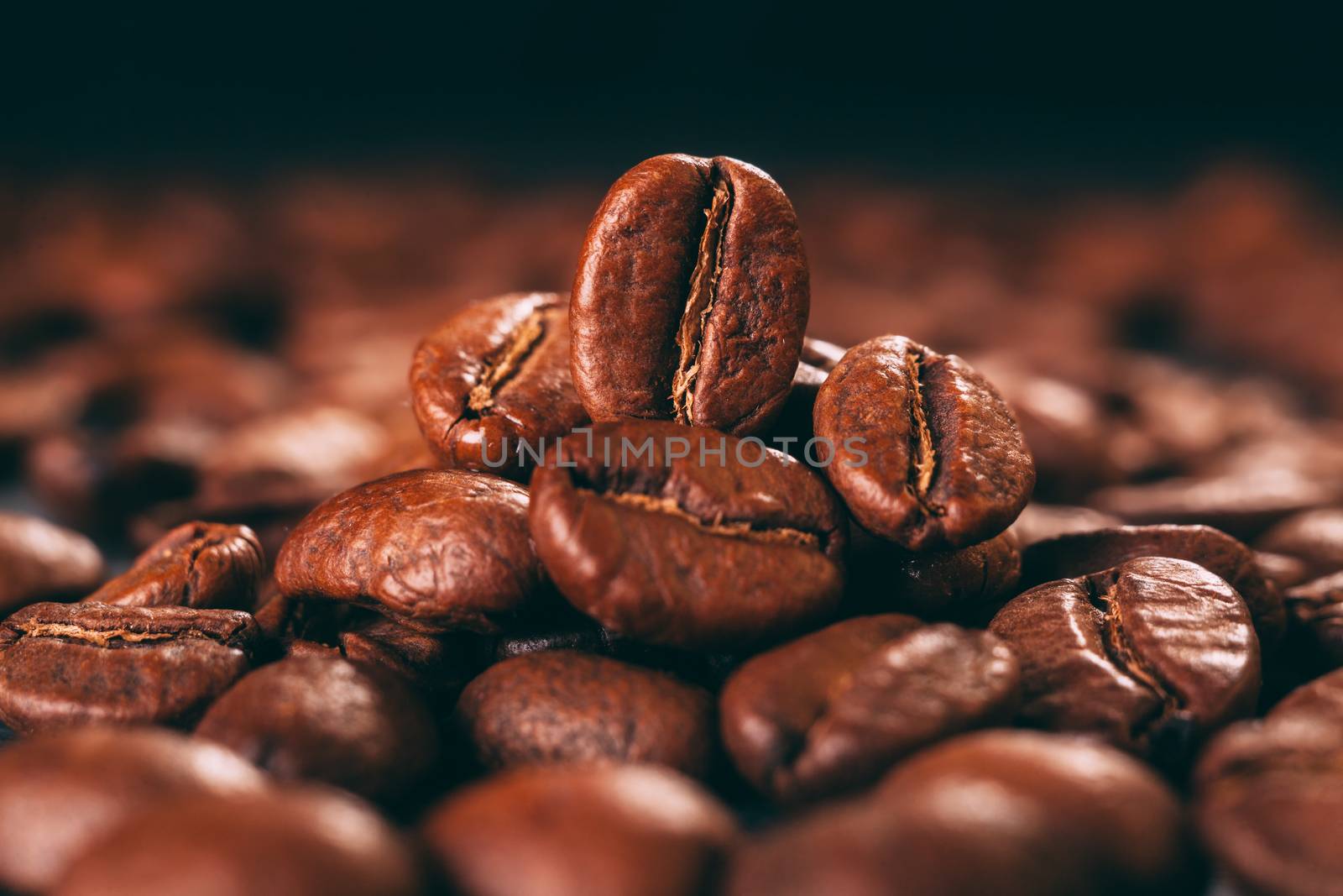 Grains of black coffee on a black granite countertop with yellow light from behind. Advertising photo of coffee. Pour coffee. Macro photo of grains.