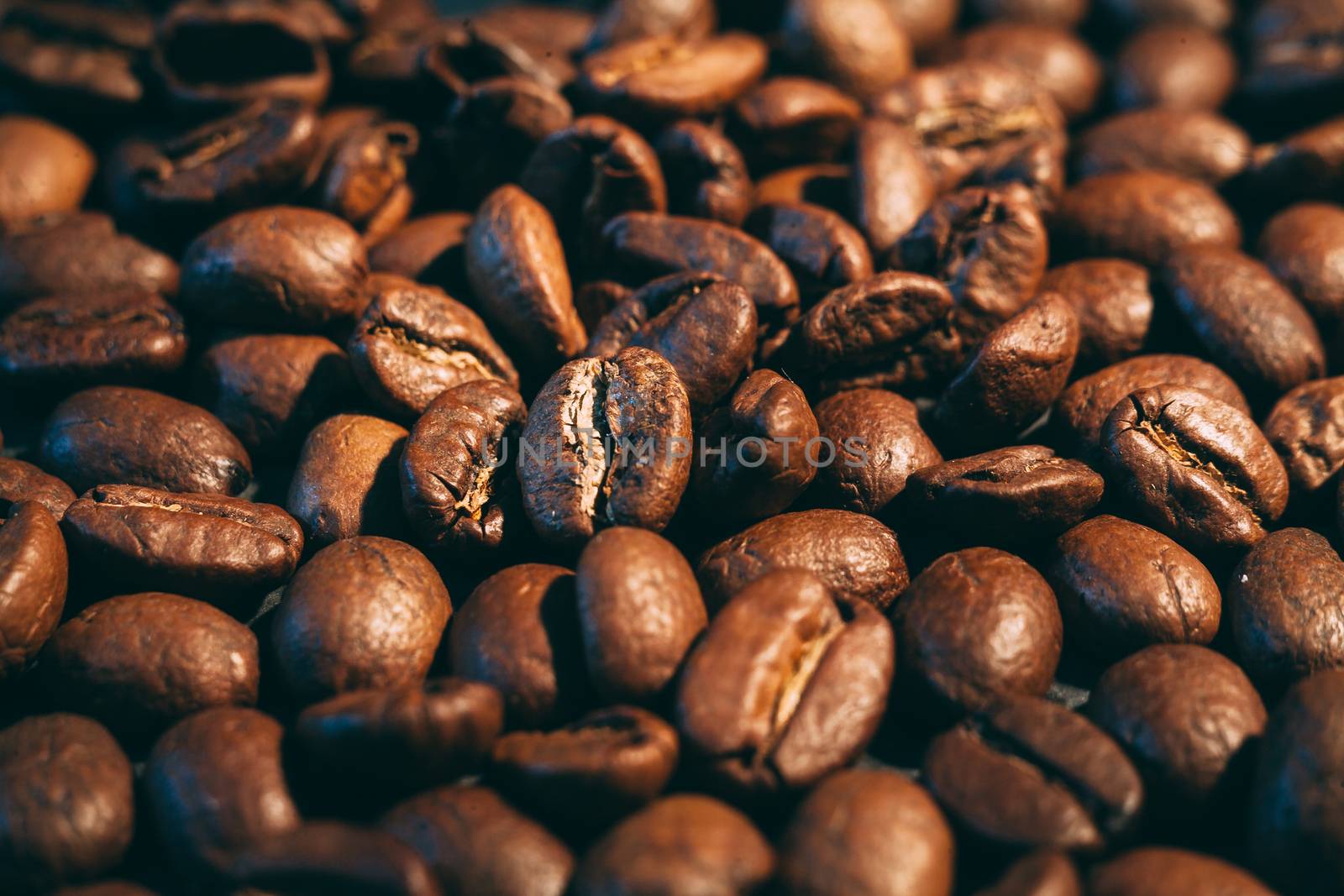 A scattering of coffee beans on a black countertop. The texture of the beans closeup. Vintage style photography.