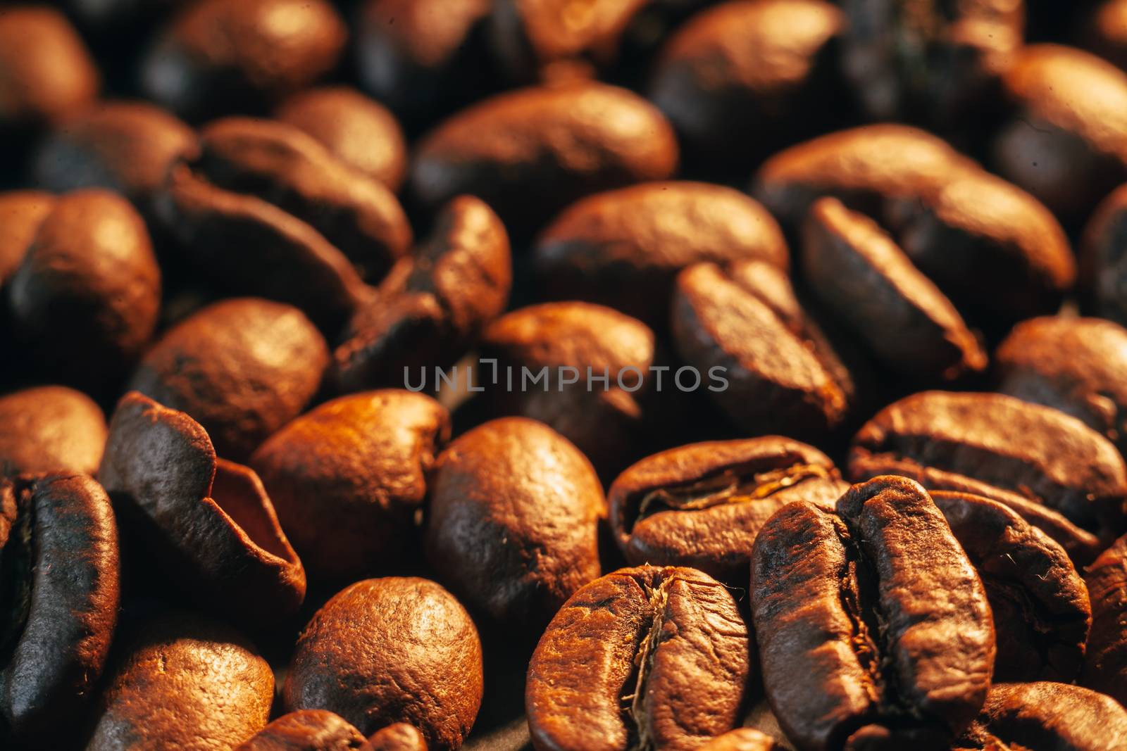 A scattering of coffee beans on a dark countertop in warm light.