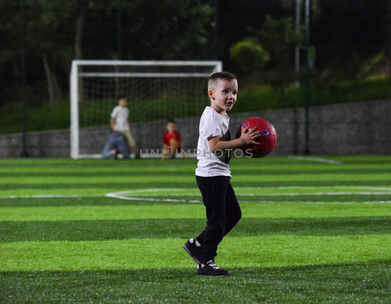 active child is playing with a red ball on the football field, night time